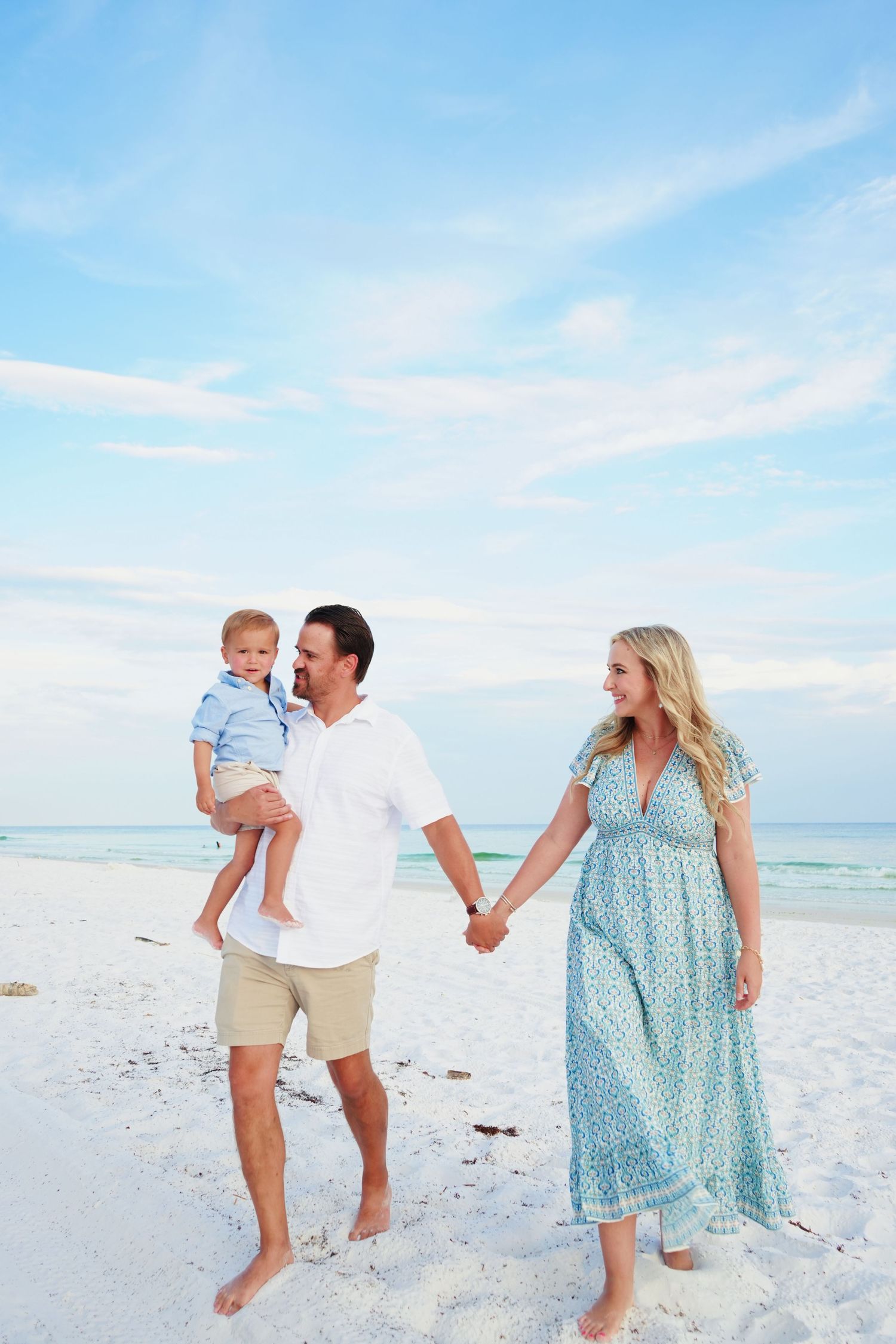 A family walks together on a pristine white sand beach under a bright blue sky.