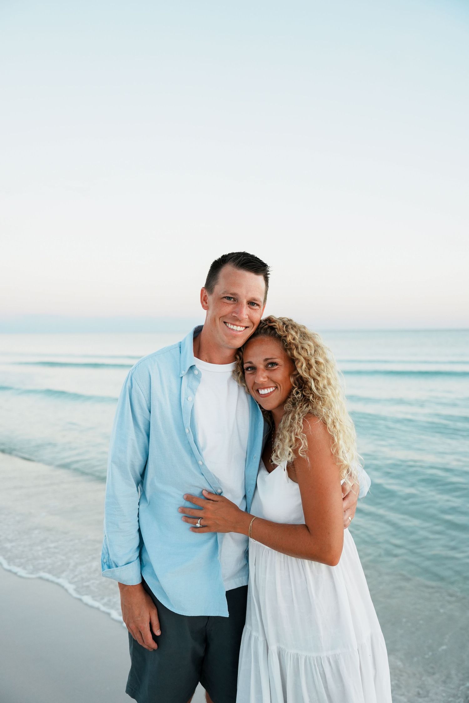 A couple shares a tender moment together on a beach with turquoise waters and soft sand in the background.