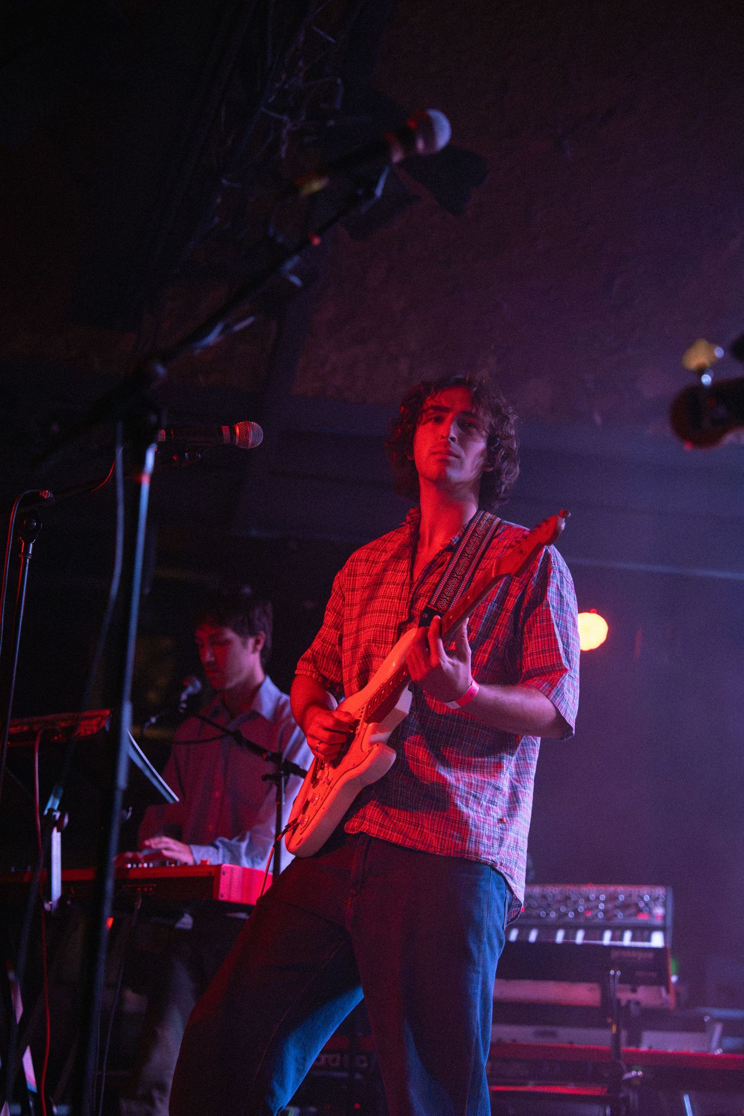 Musicians perform on a dark stage illuminated by dramatic red lighting during a live concert performance.
