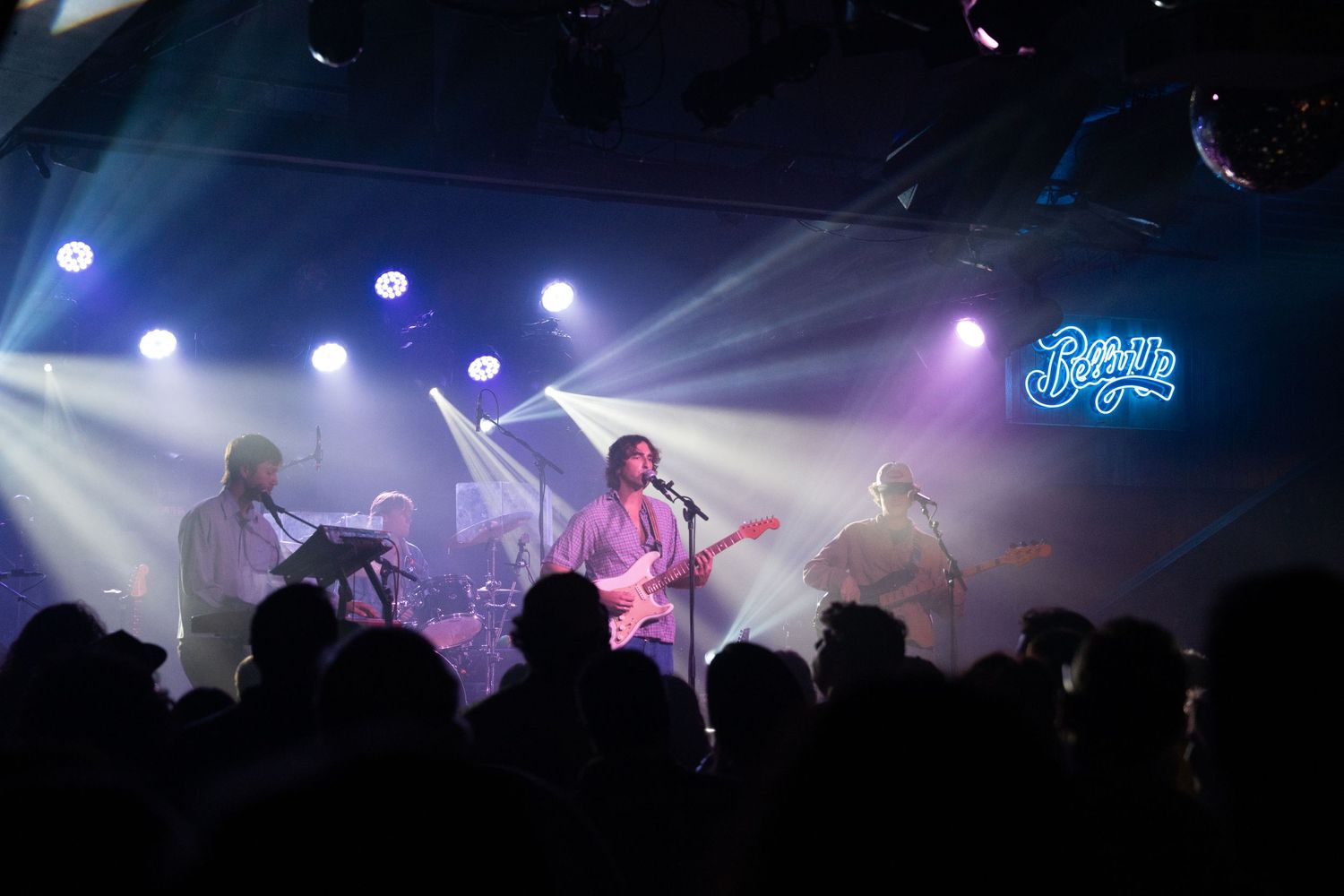 Concert crowd silhouettes against a stage with blue and purple lighting effects during a live performance.