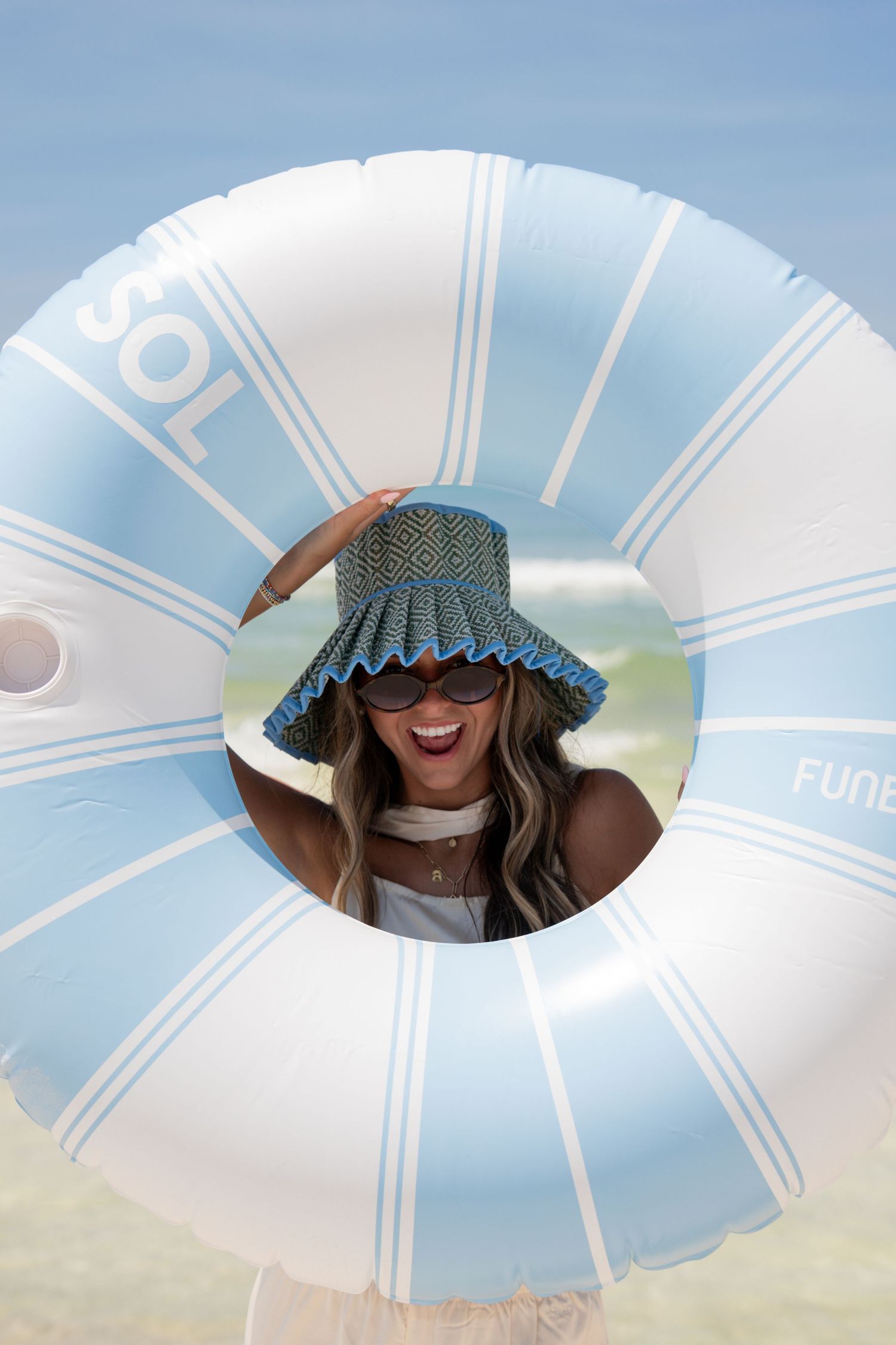 Woman smiling through a blue and white SOL inflatable pool float ring at the beach.