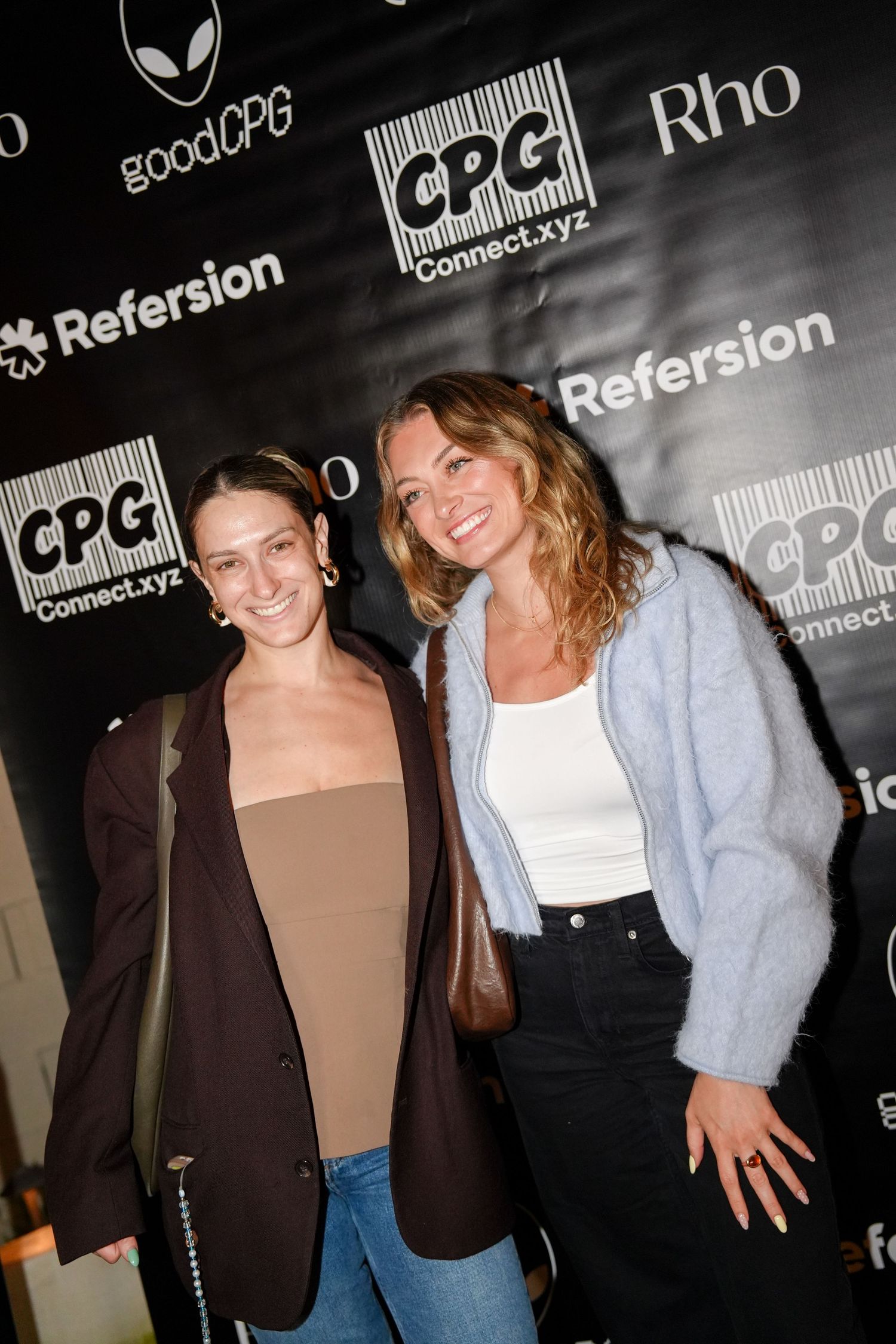 Two people posing in front of a black backdrop with CPG and other company logos at an event.