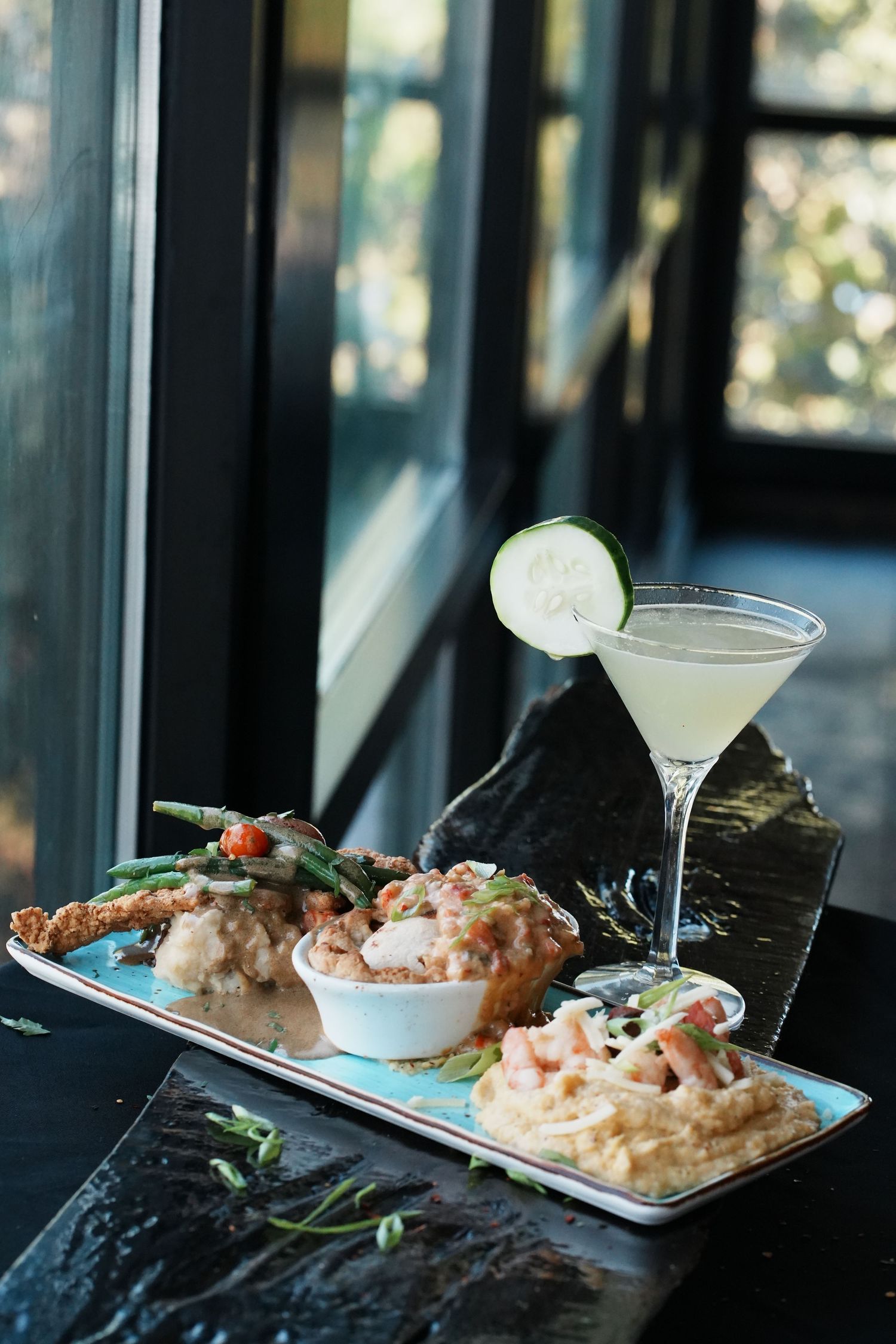 Elegant seafood dishes and cocktails arranged on a dark table by a window.