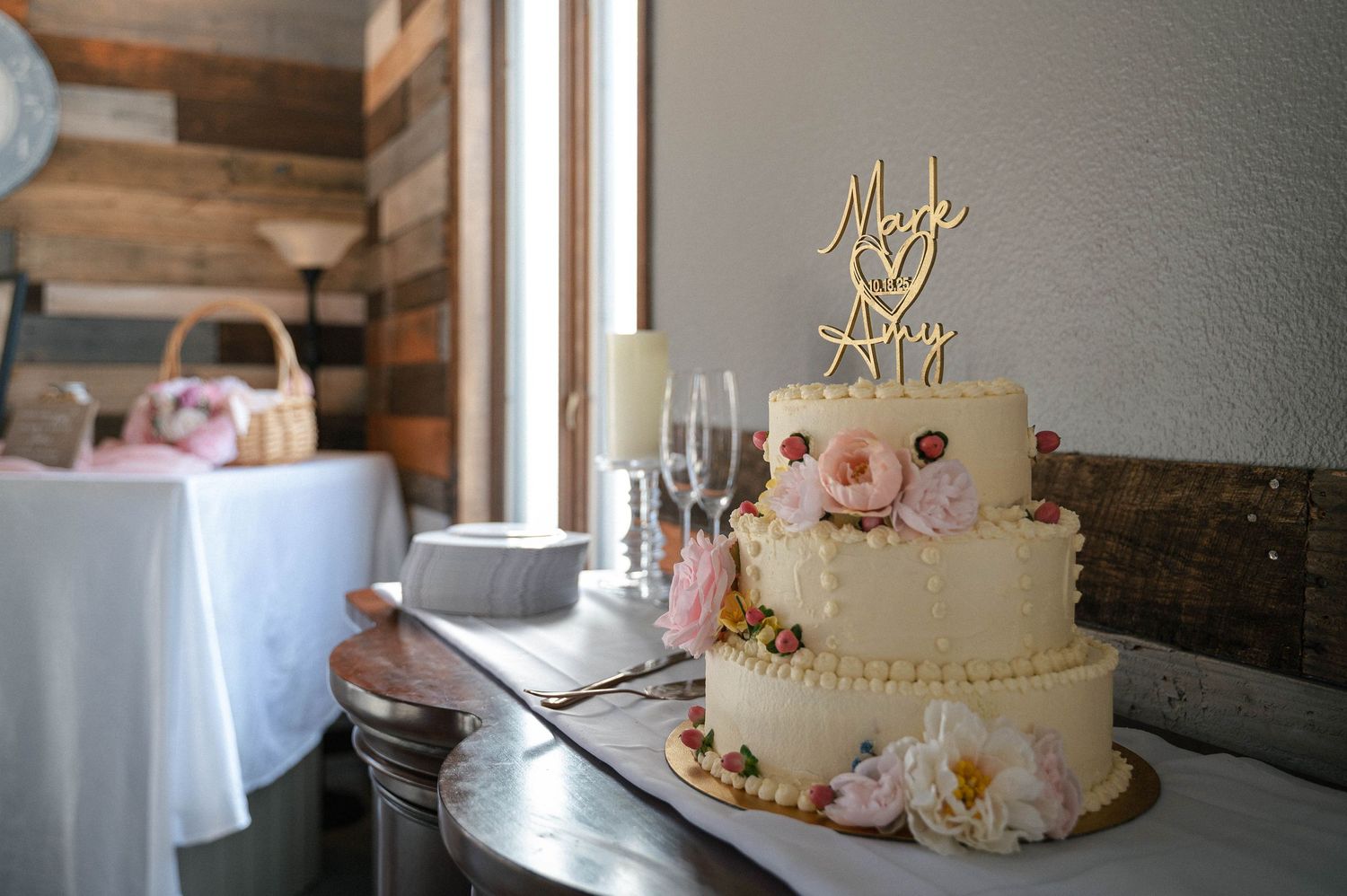 Elegant white wedding cake decorated with delicate flowers displayed near a window.