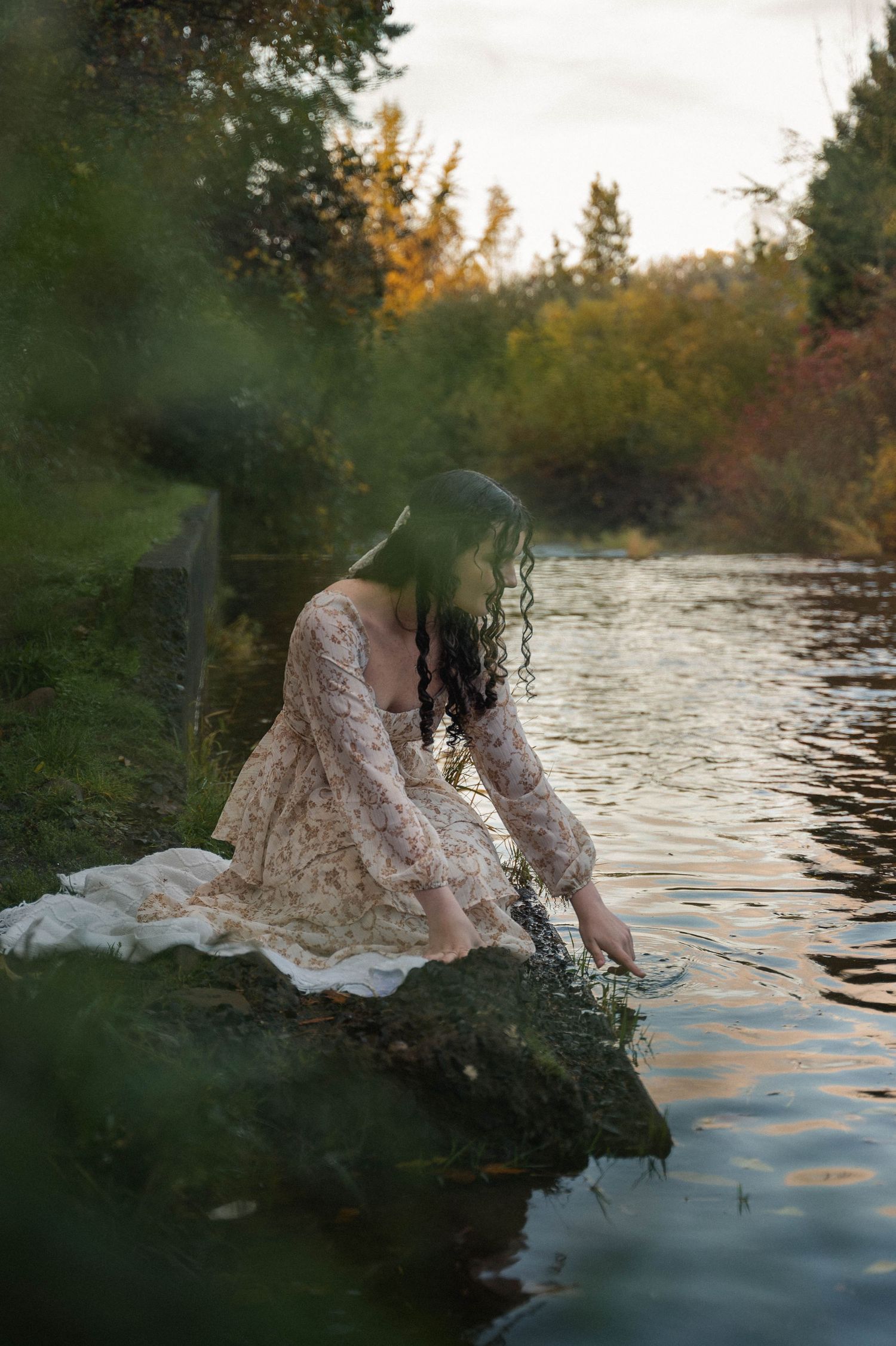 Girl sitting next to creek, dipping her finger in the water in Silverton, Oregon.