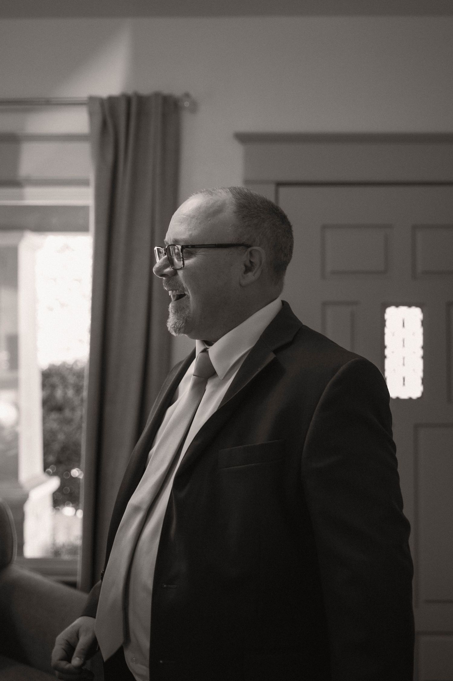 Black and white photo of a businessman in a suit and glasses smiling in an indoor setting.