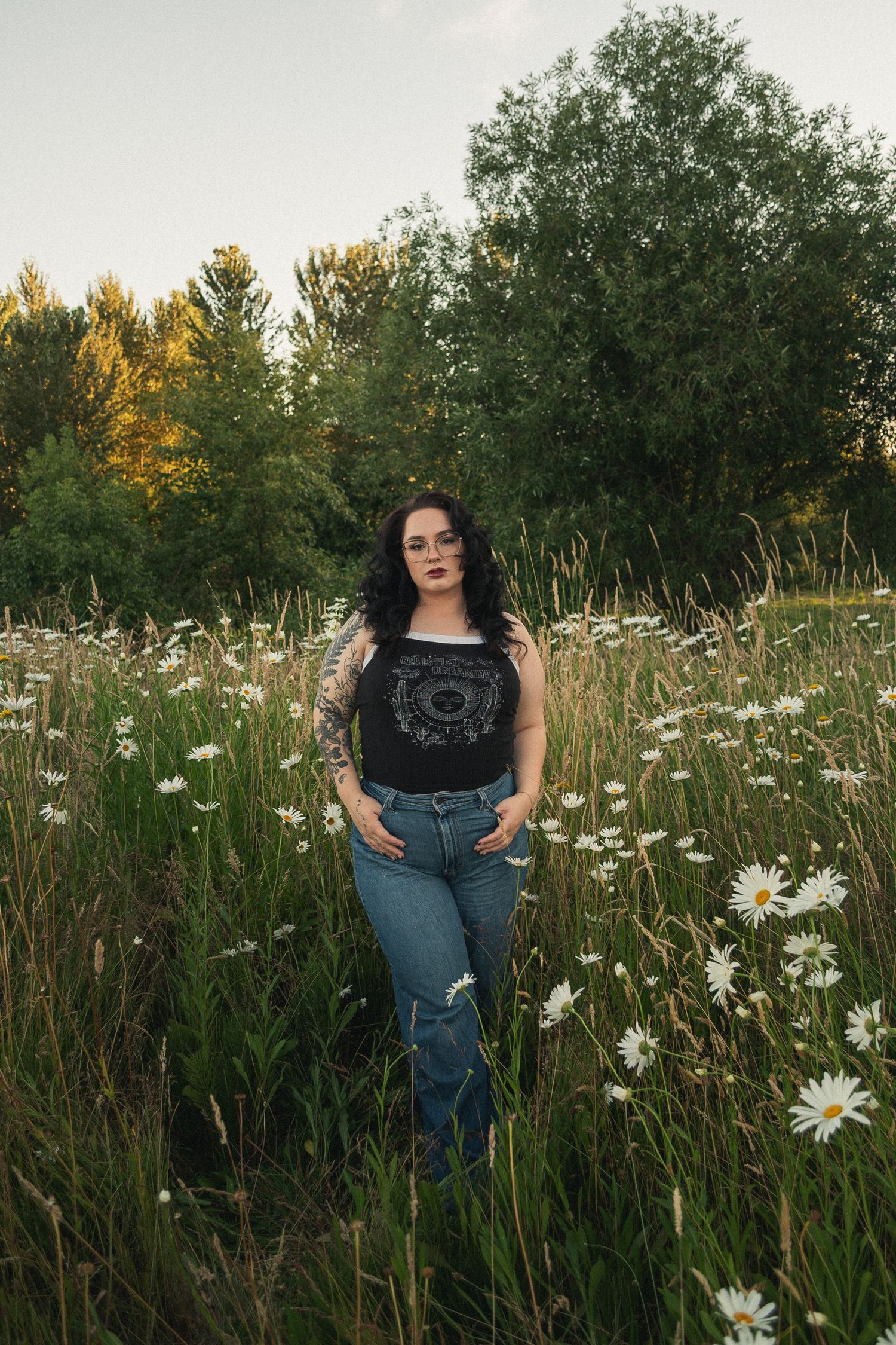 Woman in casual attire poses confidently in a field of wild daisies at sunset.