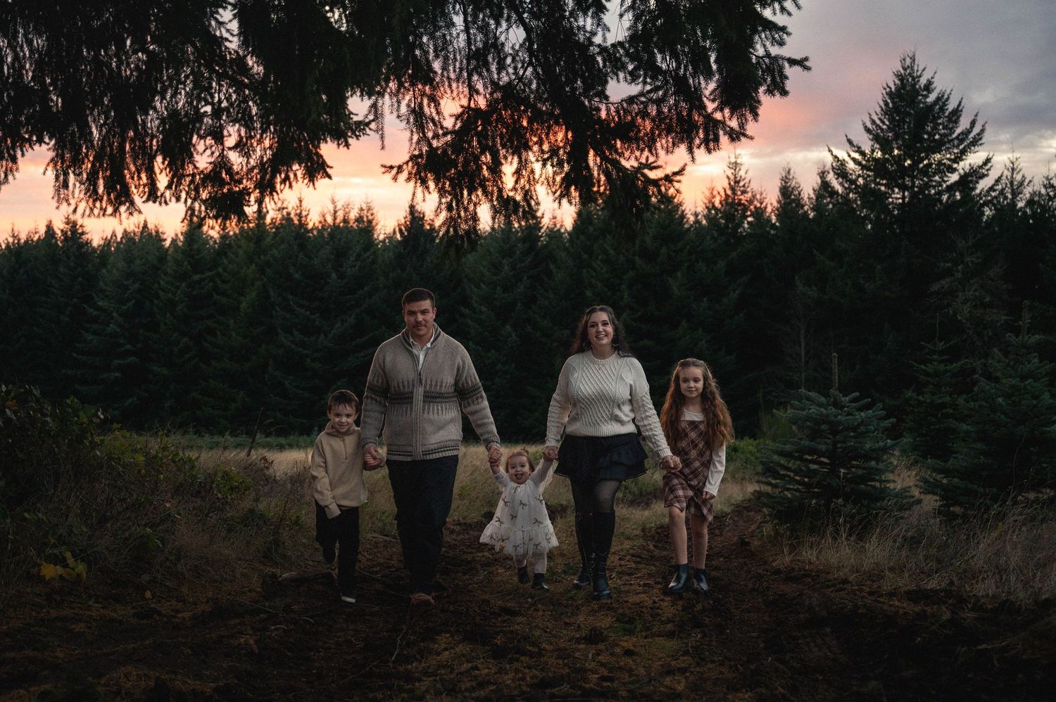 A group walks together on a forest path at sunset with evergreen trees silhouetted in the background.