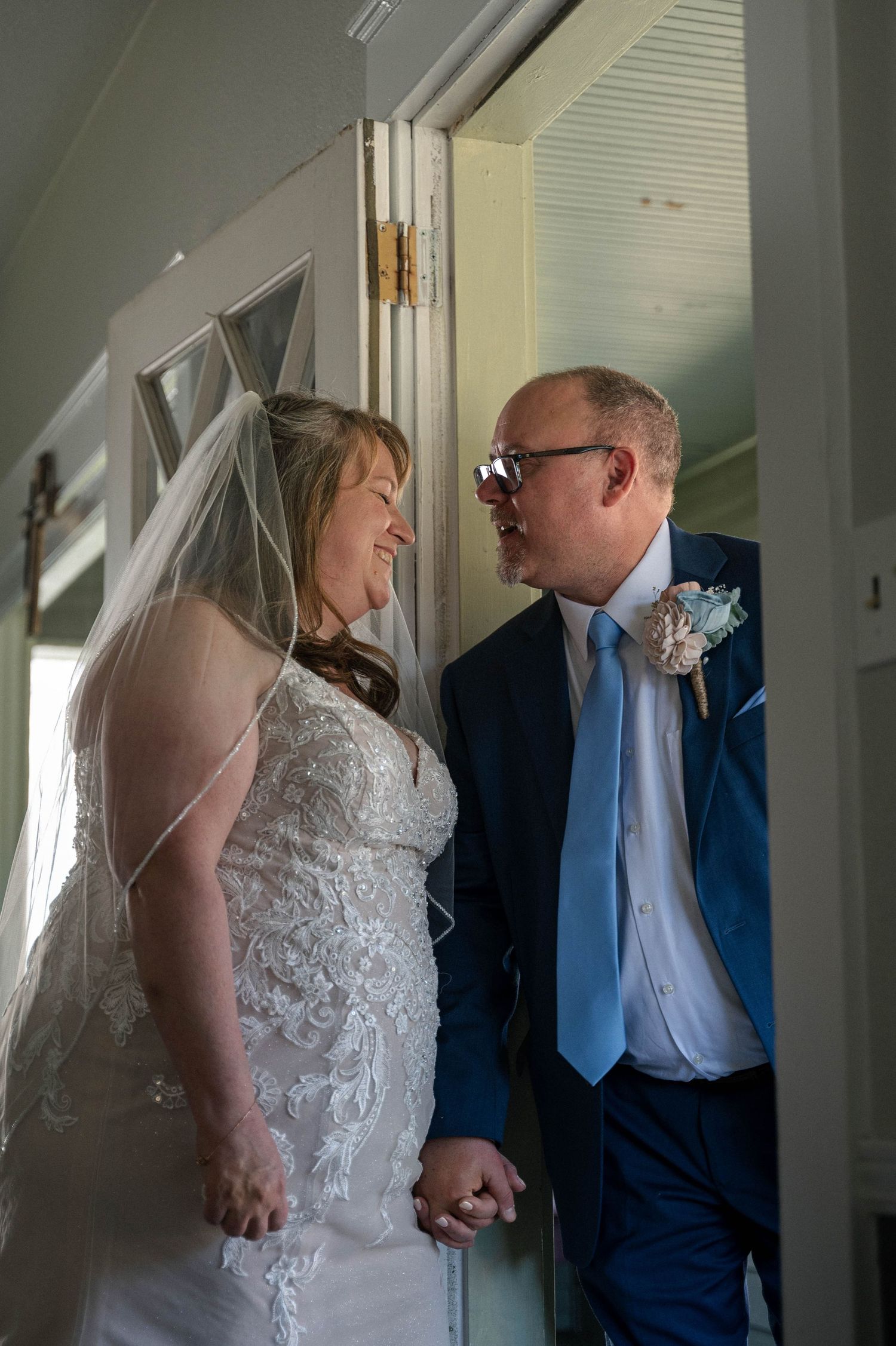 A bride and groom share an intimate moment in a doorway, with the bride wearing a lace gown and veil.