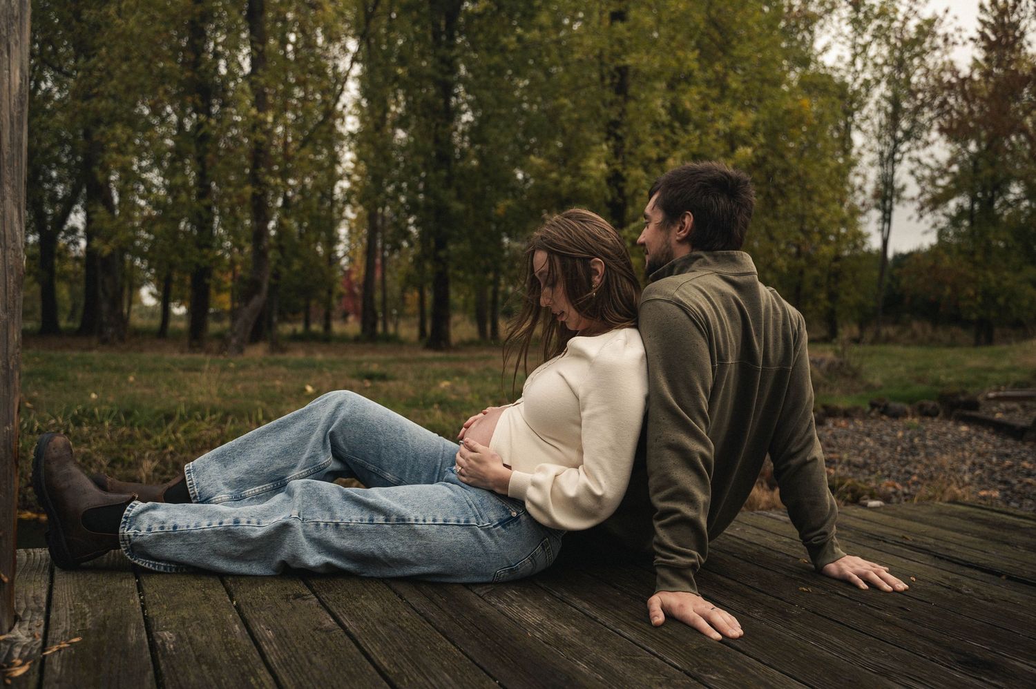 Pregnant woman and husband sitting close on a dock, feet hanging over the pond in Silverton, Oregon.