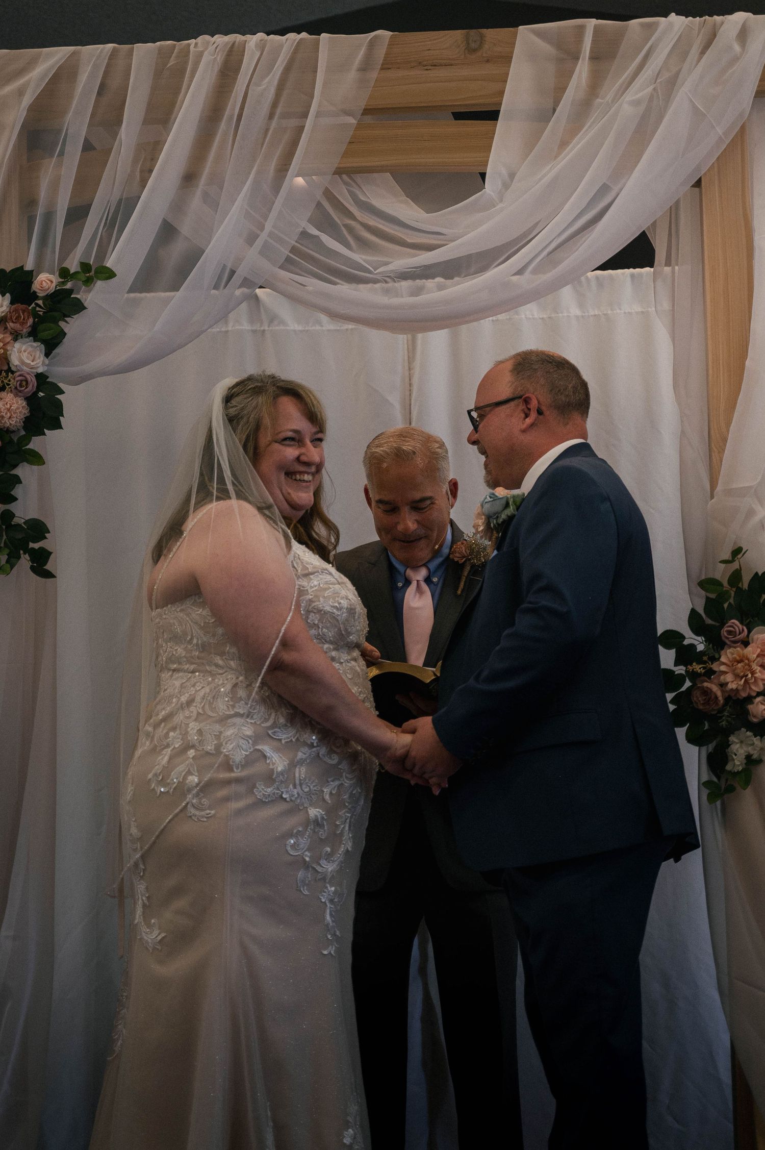 Wedding ceremony taking place under white draped fabric with floral decorations.