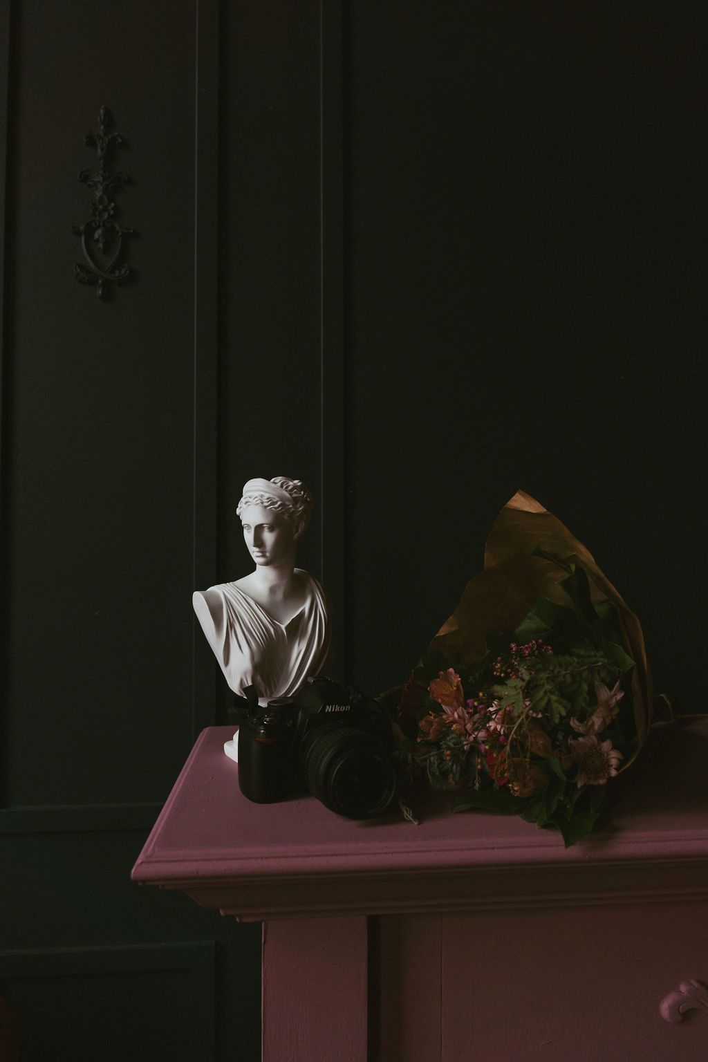 moody antique statue set on a pink mantle next to a bouquet of flowers and a camera in Salem Oregon