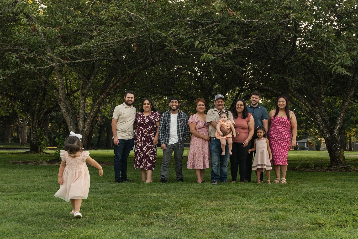 A group of people stand together outdoors in a grassy park area on a sunny day.