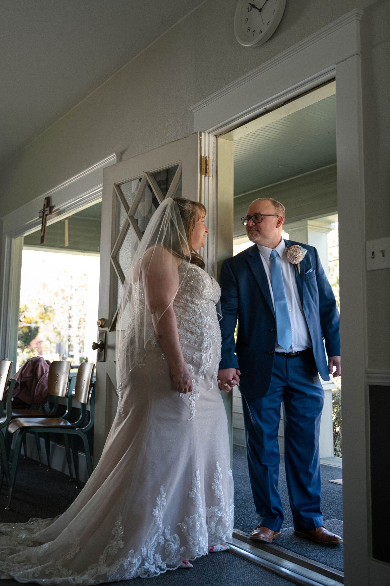 Wedding attire with white lace dress and navy suit seen in bright indoor venue.