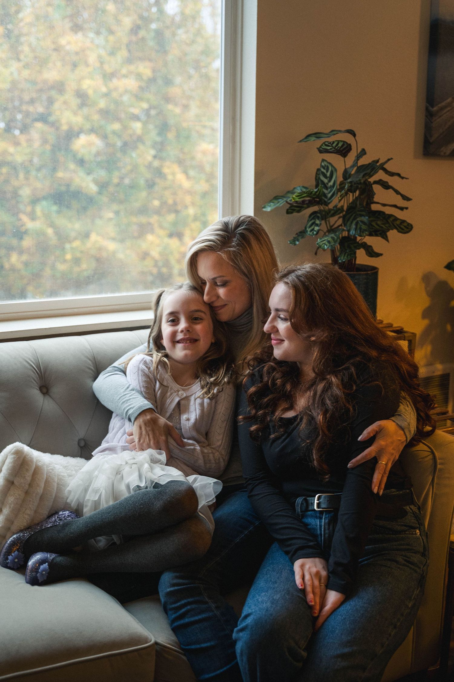 Mother and two daughters sitting close, next to the fire in their living room.