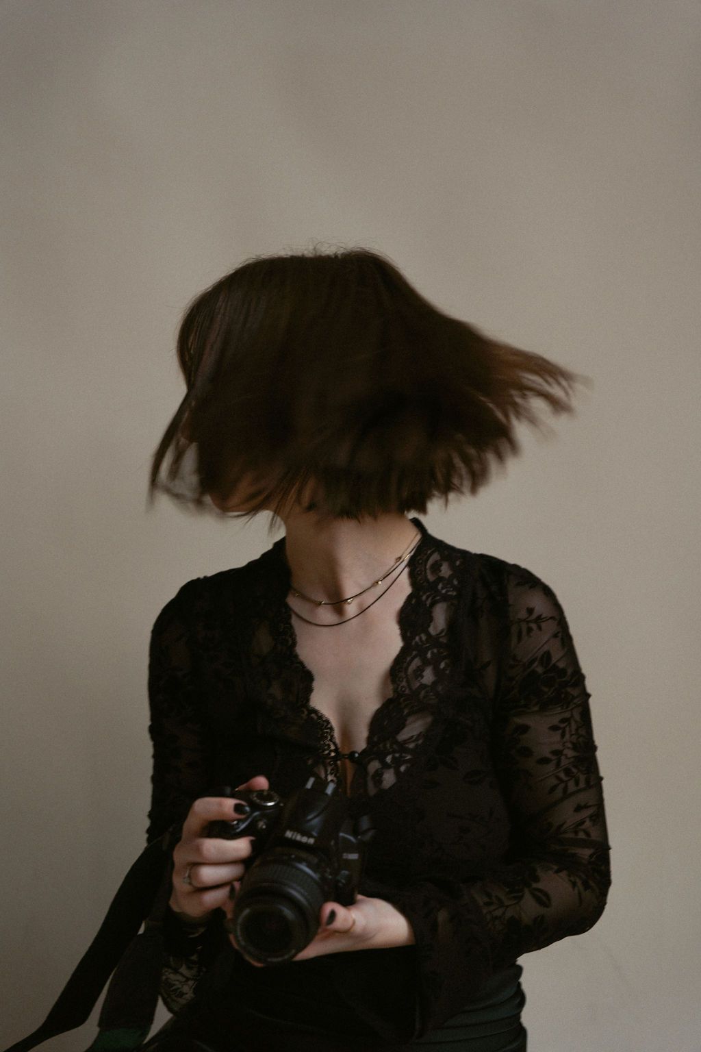 Woman dressed in black, holding a camera while shaking her head, her hair is a blur