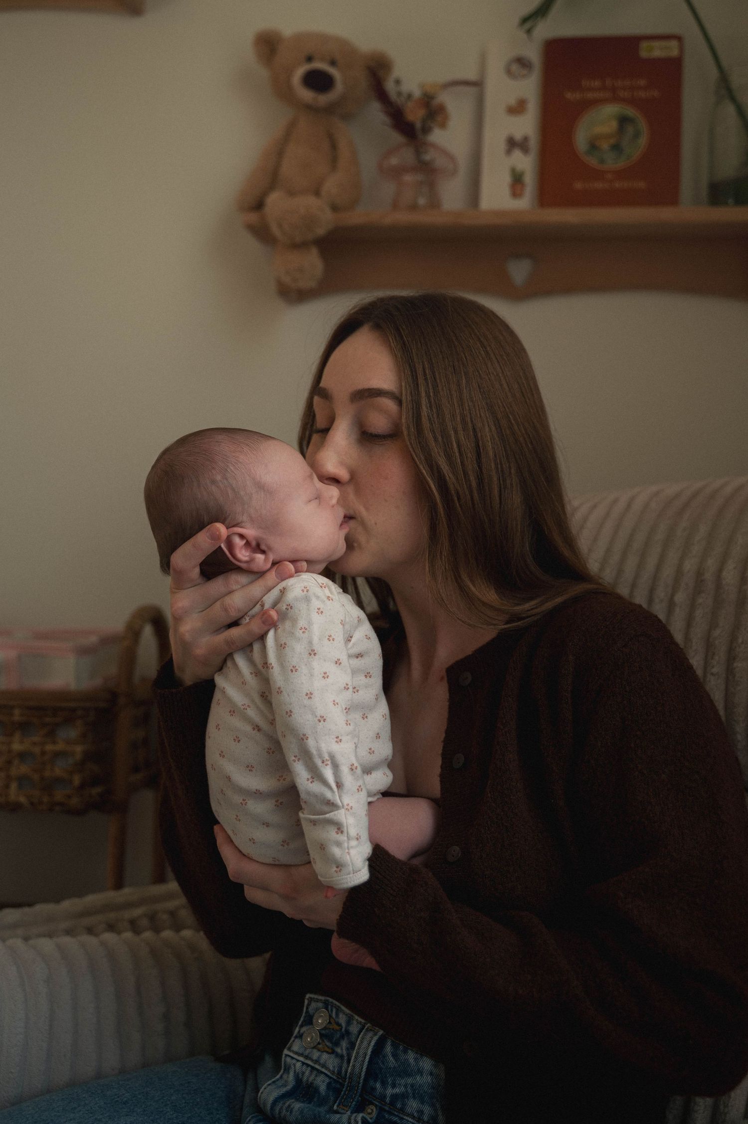 A tender moment shows a parent giving loving kisses to a baby wearing a white onesie while sitting on a couch.