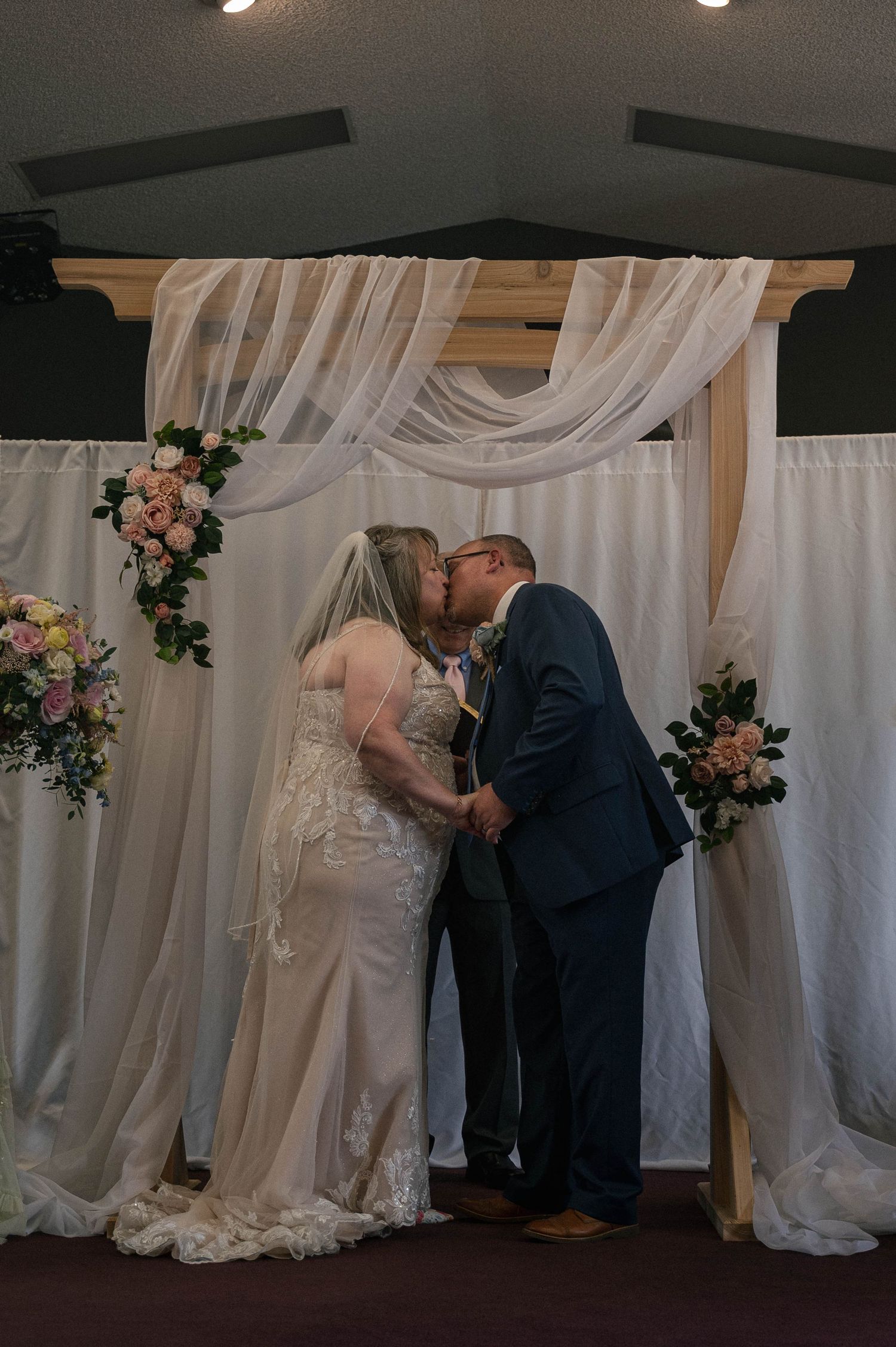 Wedding ceremony setup with white fabric draped arbor and pink floral accents.