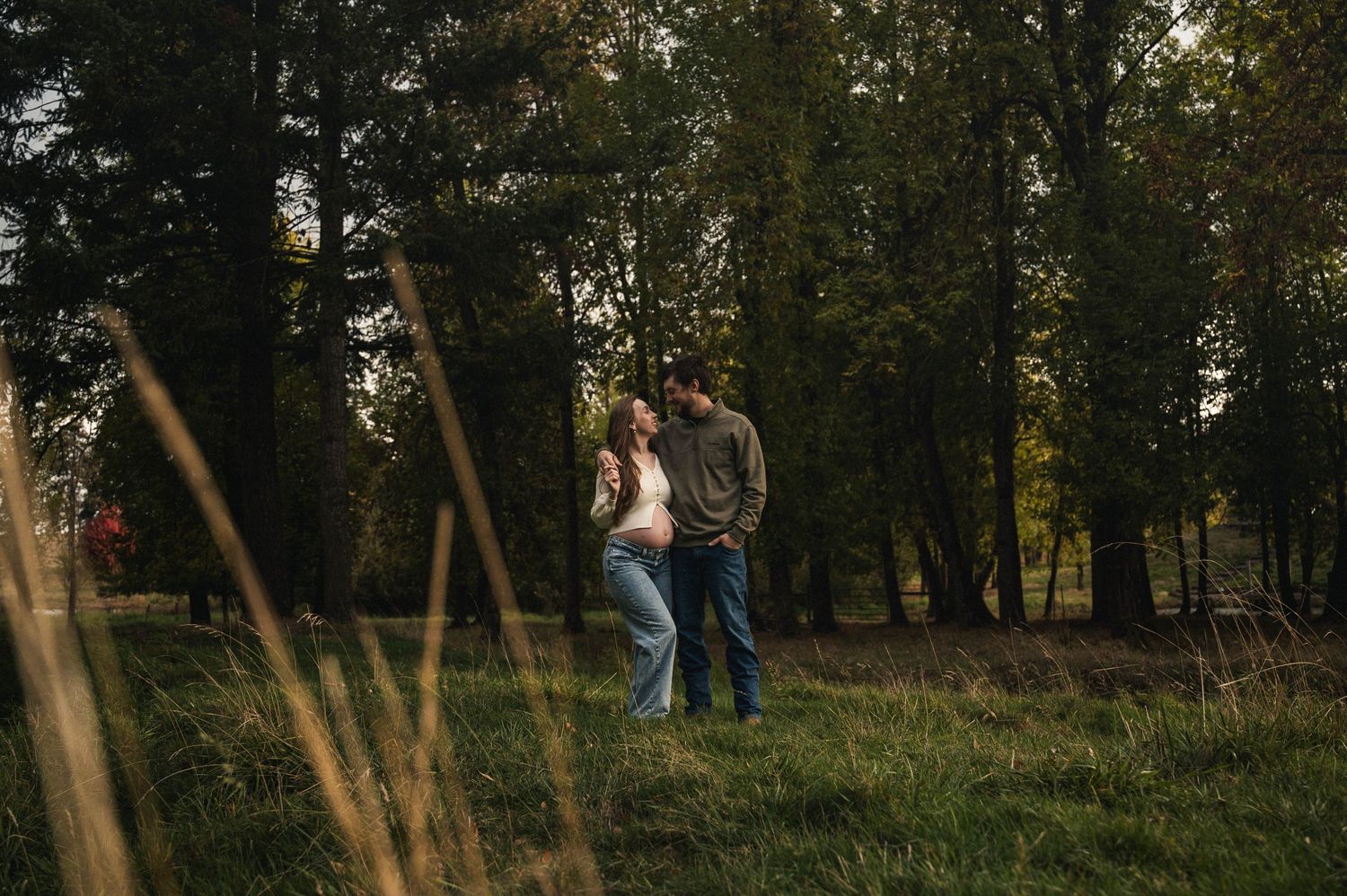 A couple walks together through a wooded area during golden hour as sunlight filters through the trees.