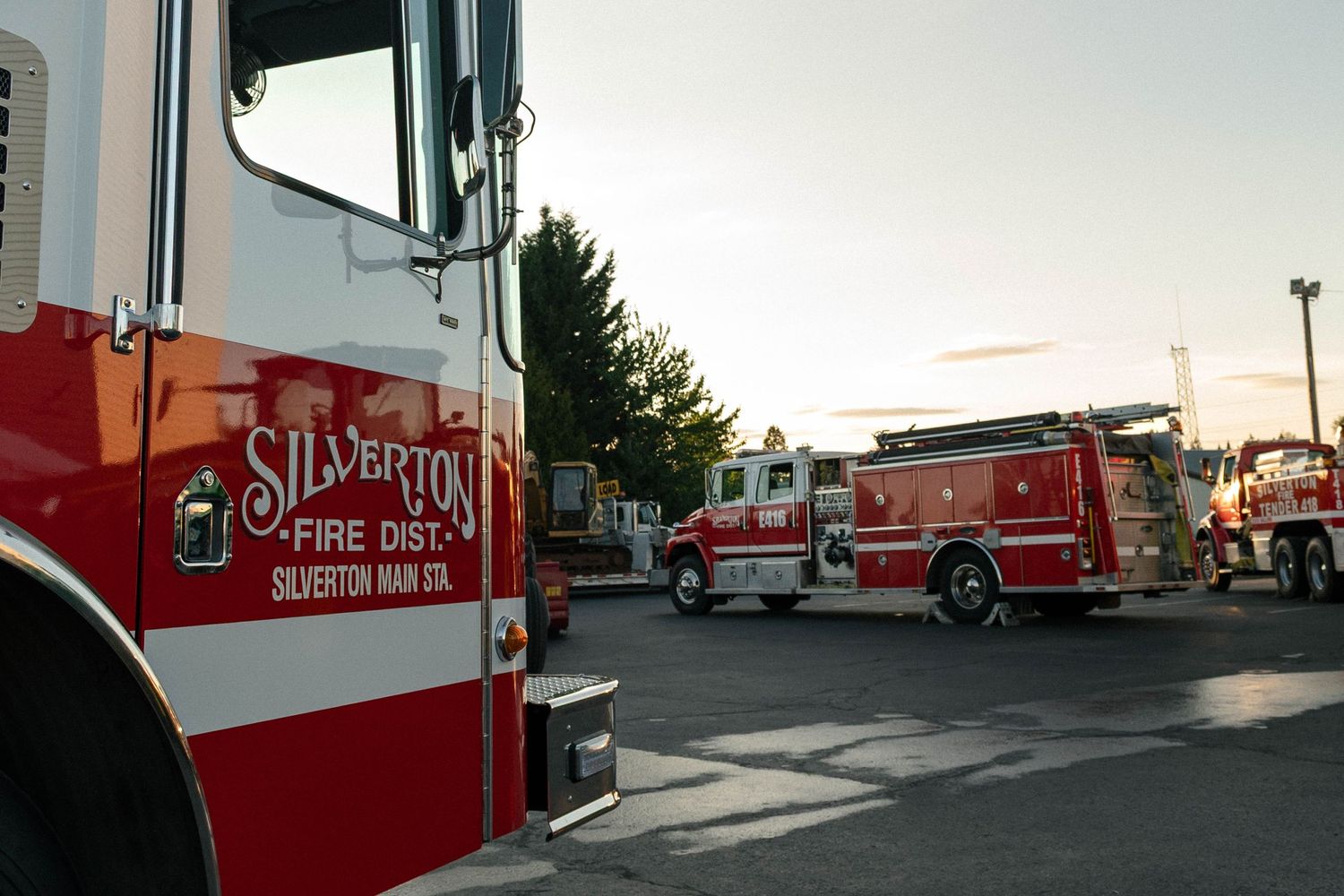 A series of fire trucks and emergency vehicles parked at a station during sunset.