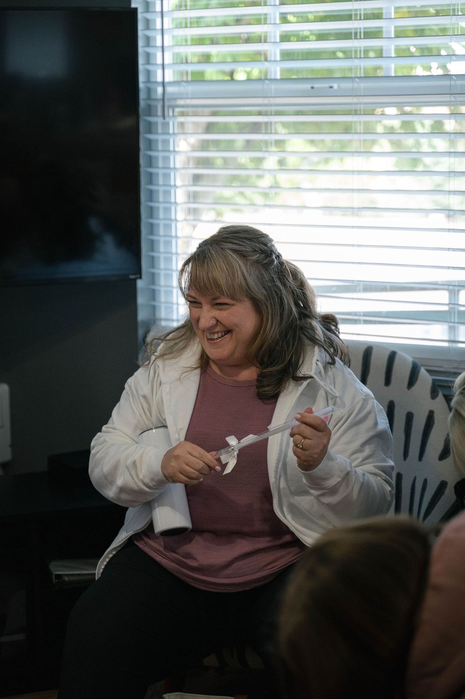 A sequence of photos showing someone in a white jacket expressing joyful laughter while seated indoors by a window.