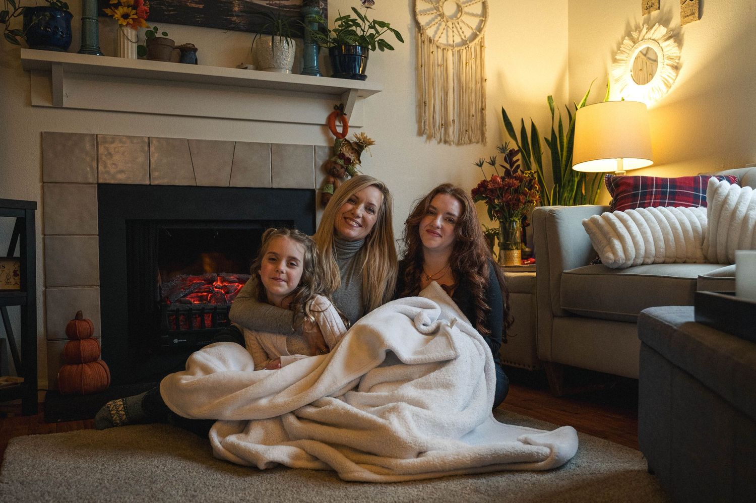 Mother and two daughters sitting close, next to the fire in their living room.