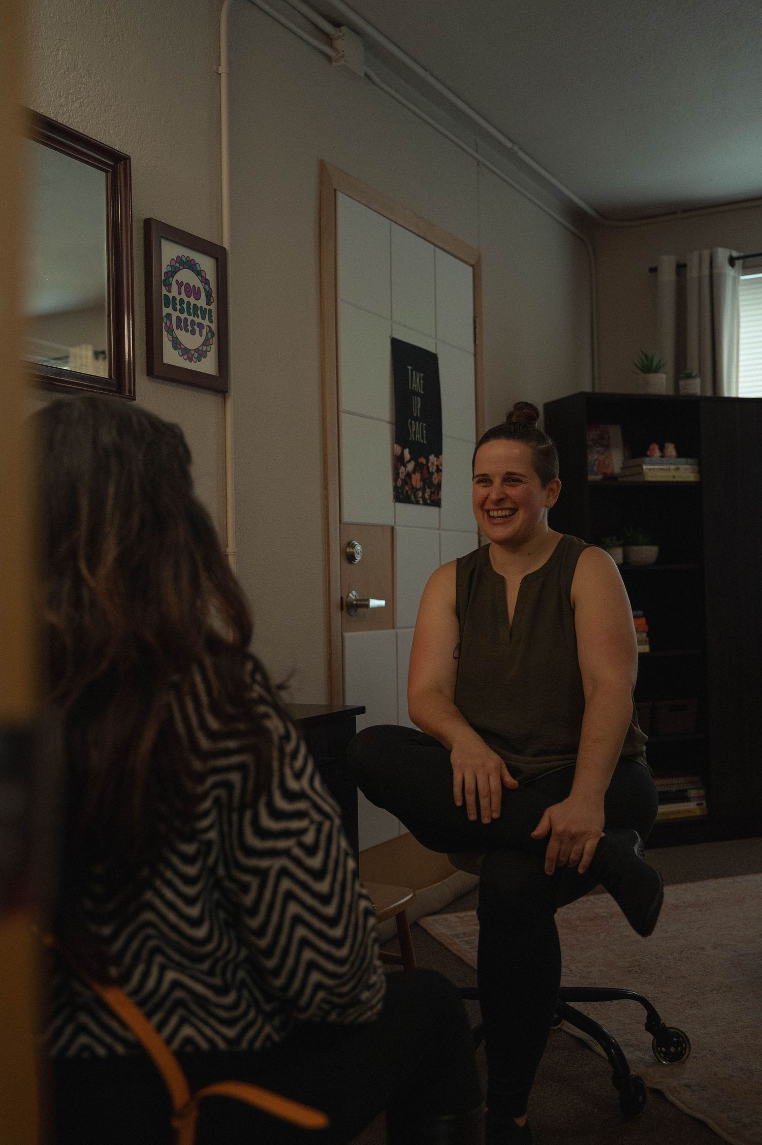 Two people sit in a dimly lit room having an animated conversation.