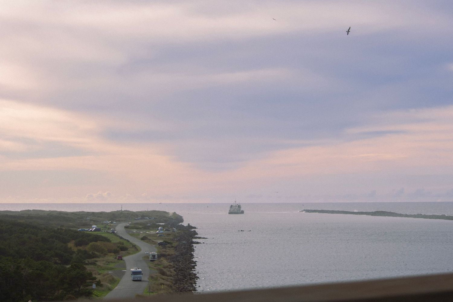a ship next to the Oregon coastline, where a road with a camper van follows at sunset by Moon Street Photography