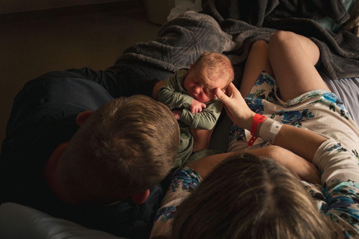 couple sits in hospital bed holding brand new baby by Moon Street Photography