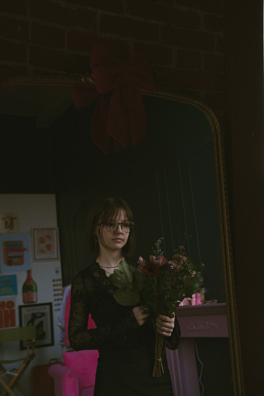 Woman holding flowers, looking at herself in a mirror dressed in black