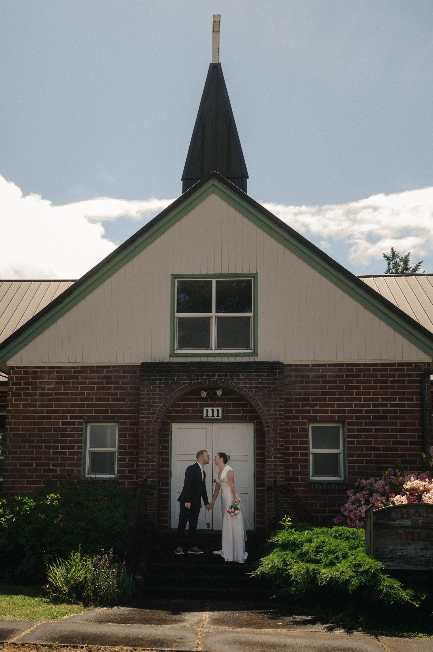 Bride and groom kiss outside brick church with steeple on wedding day.