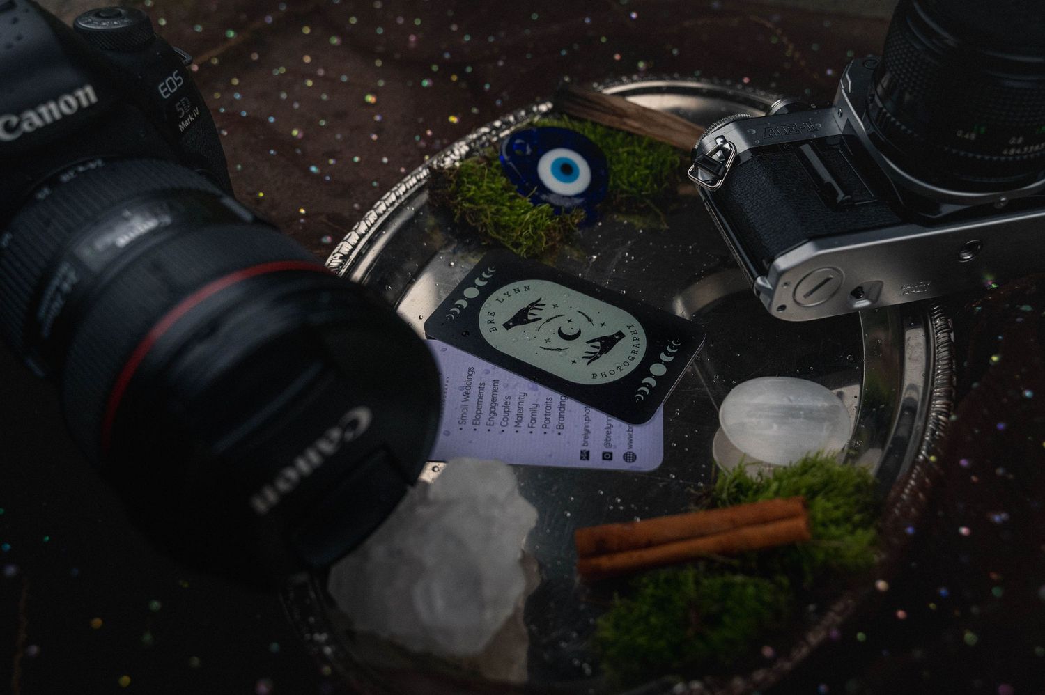 Camera equipment and lenses scattered across a dark textured surface with some greenery visible in the composition.