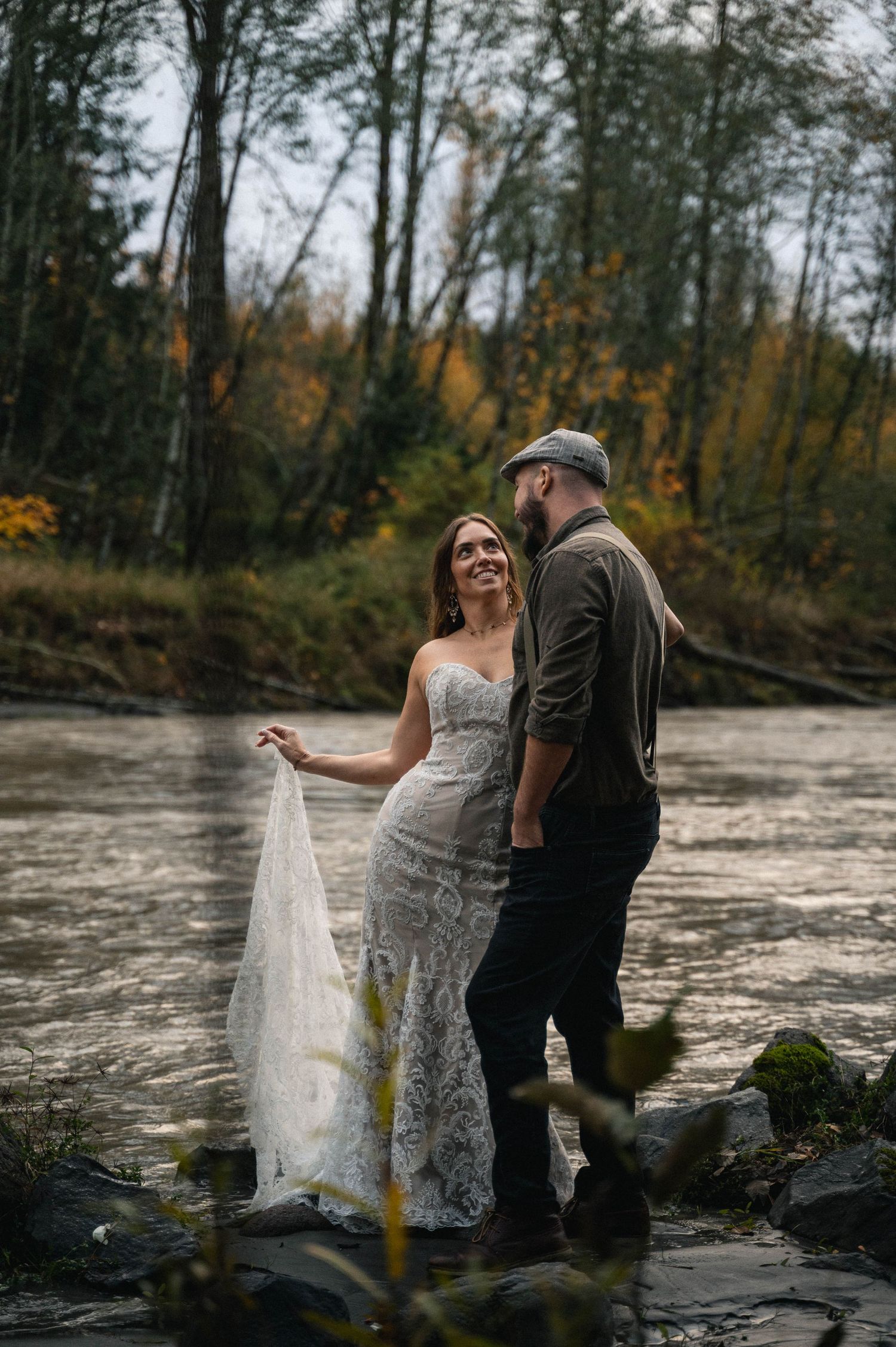 A couple embraces near a river with autumn trees creating a romantic backdrop.