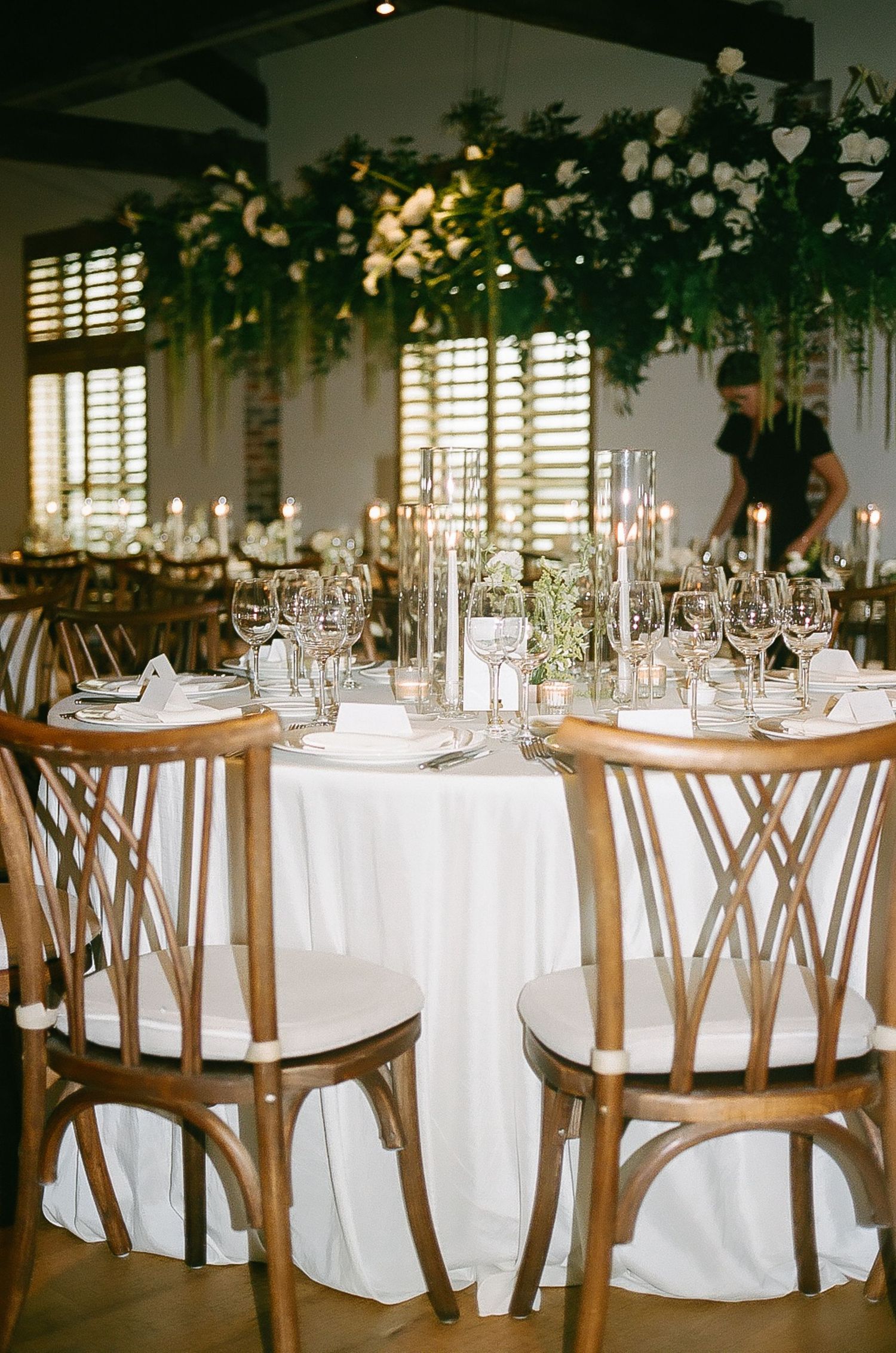 Elegant wedding reception tables set with white linens and wooden cross-back chairs.