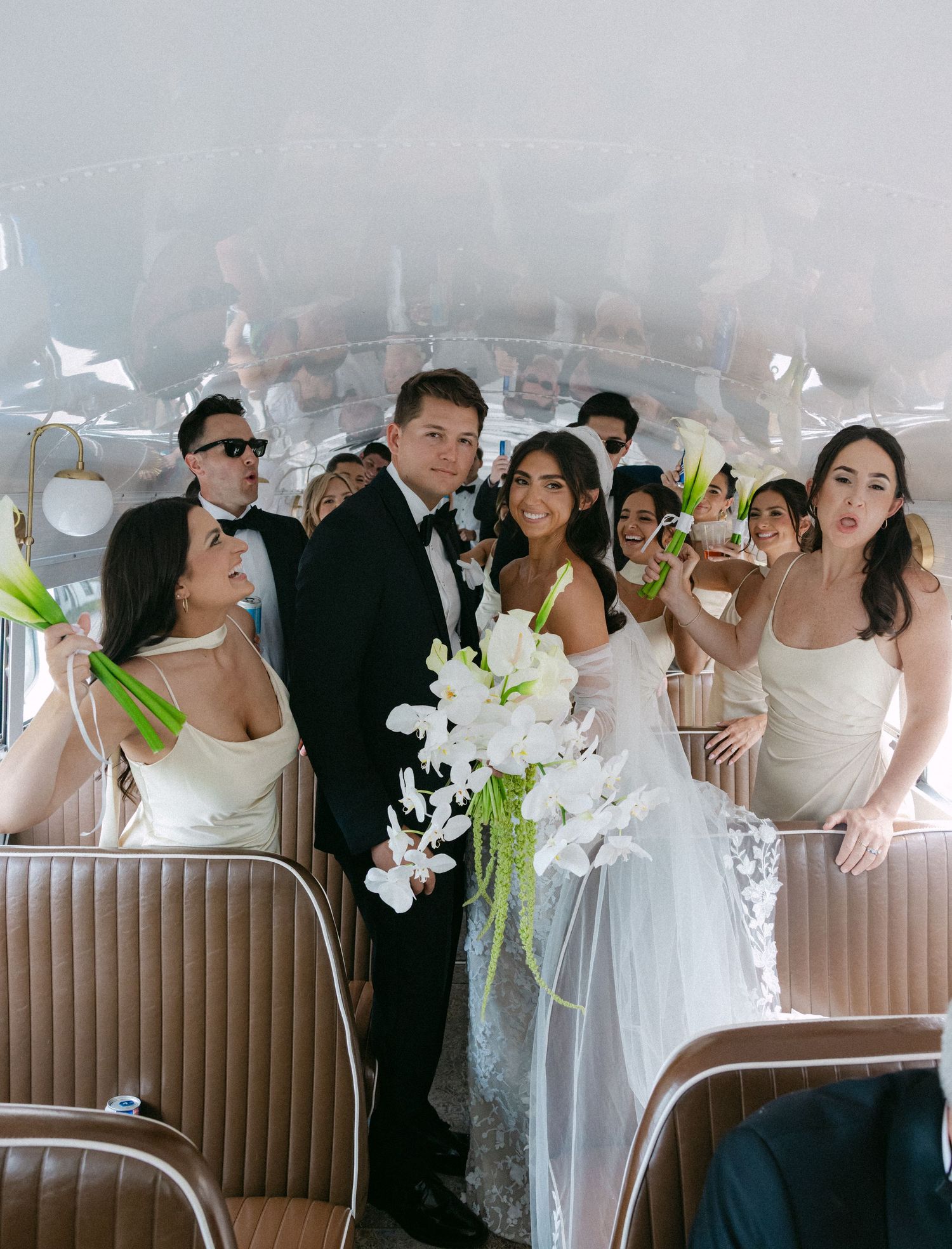 Lively wedding reception scene with guests gathered around upholstered banquette seating and floral decorations.