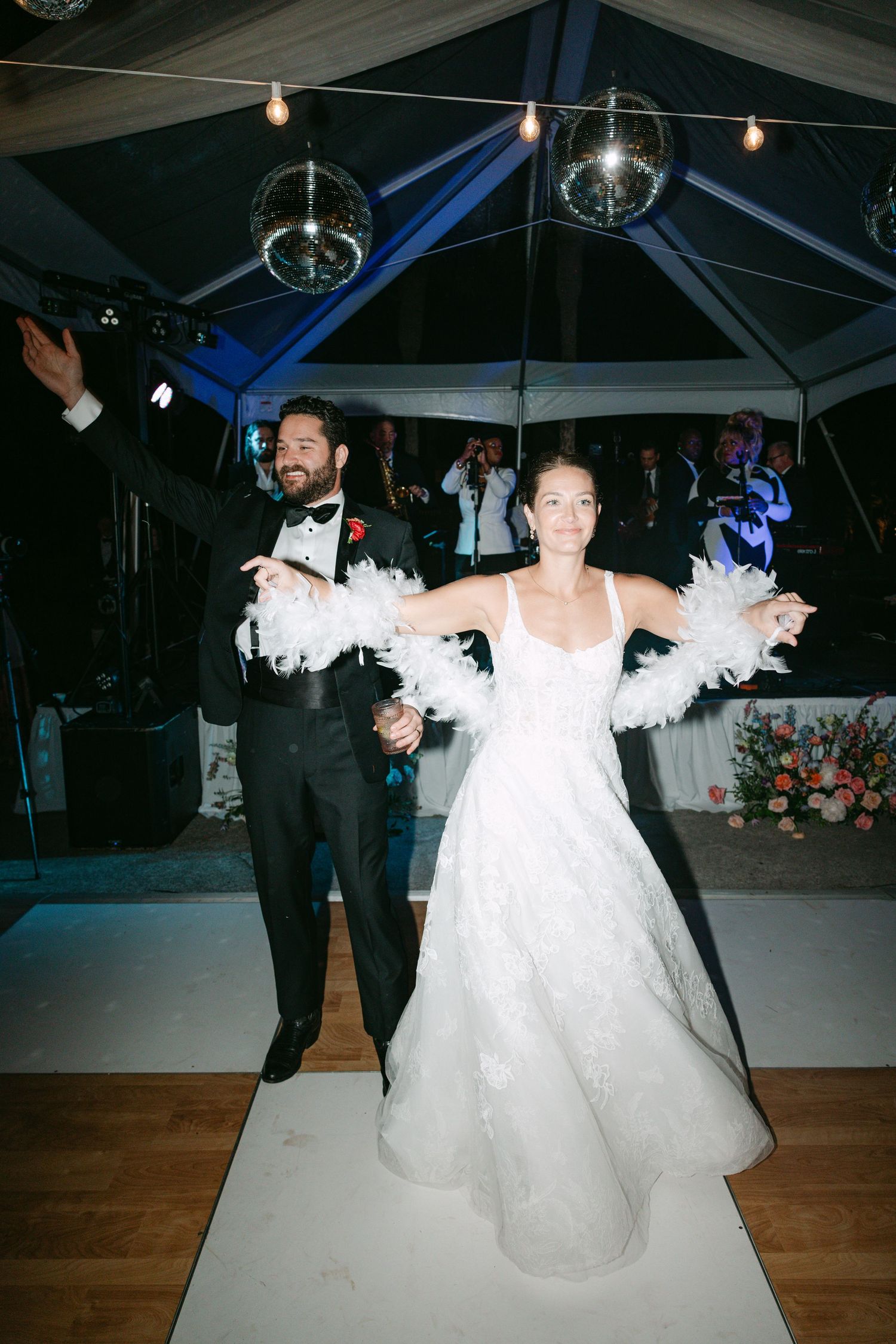 Bride in white feather bolero and groom in tuxedo make grand entrance at tented wedding reception.