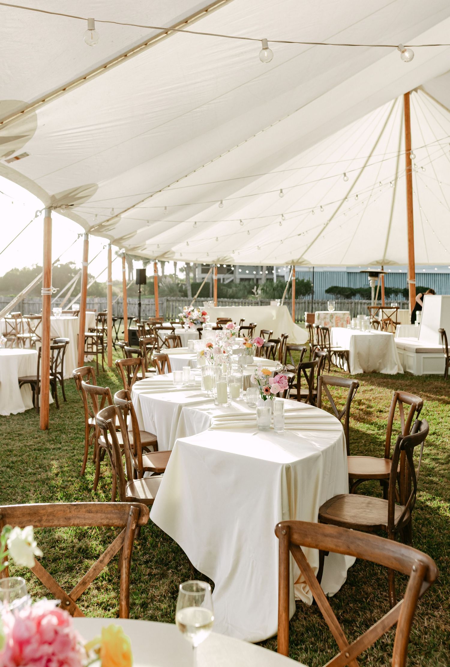Elegant outdoor wedding reception under a white sailcloth tent with string lights and floral centerpieces.