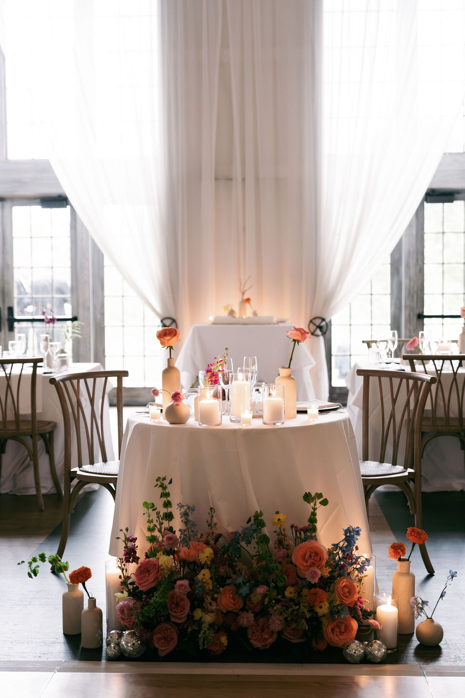 Romantic sweetheart table adorned with lush pink floral arrangements, candles, and sheer white draping at a wedding reception.
