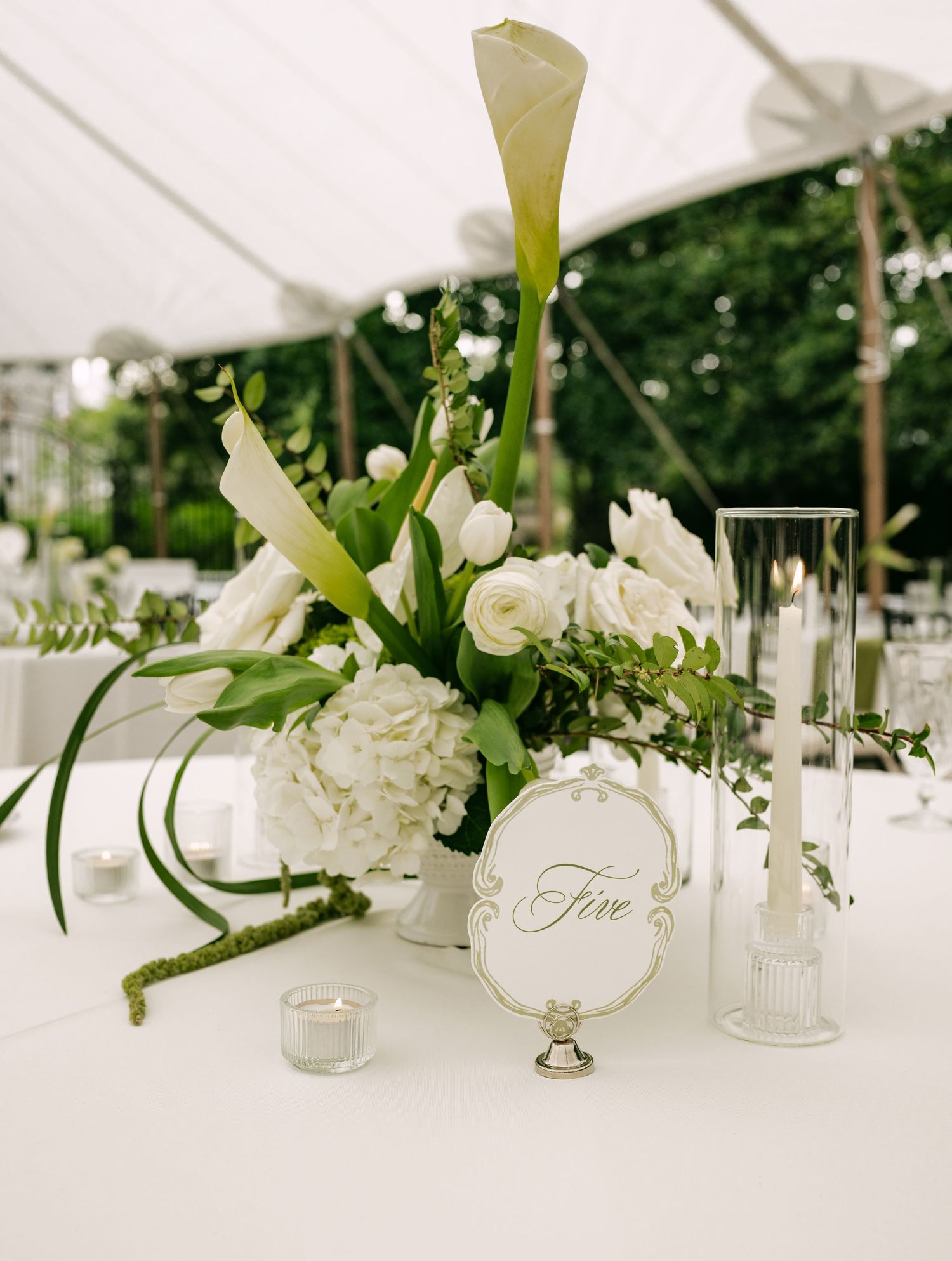 White wedding centerpiece with calla lilies, hydrangeas, and roses beside table number five sign.