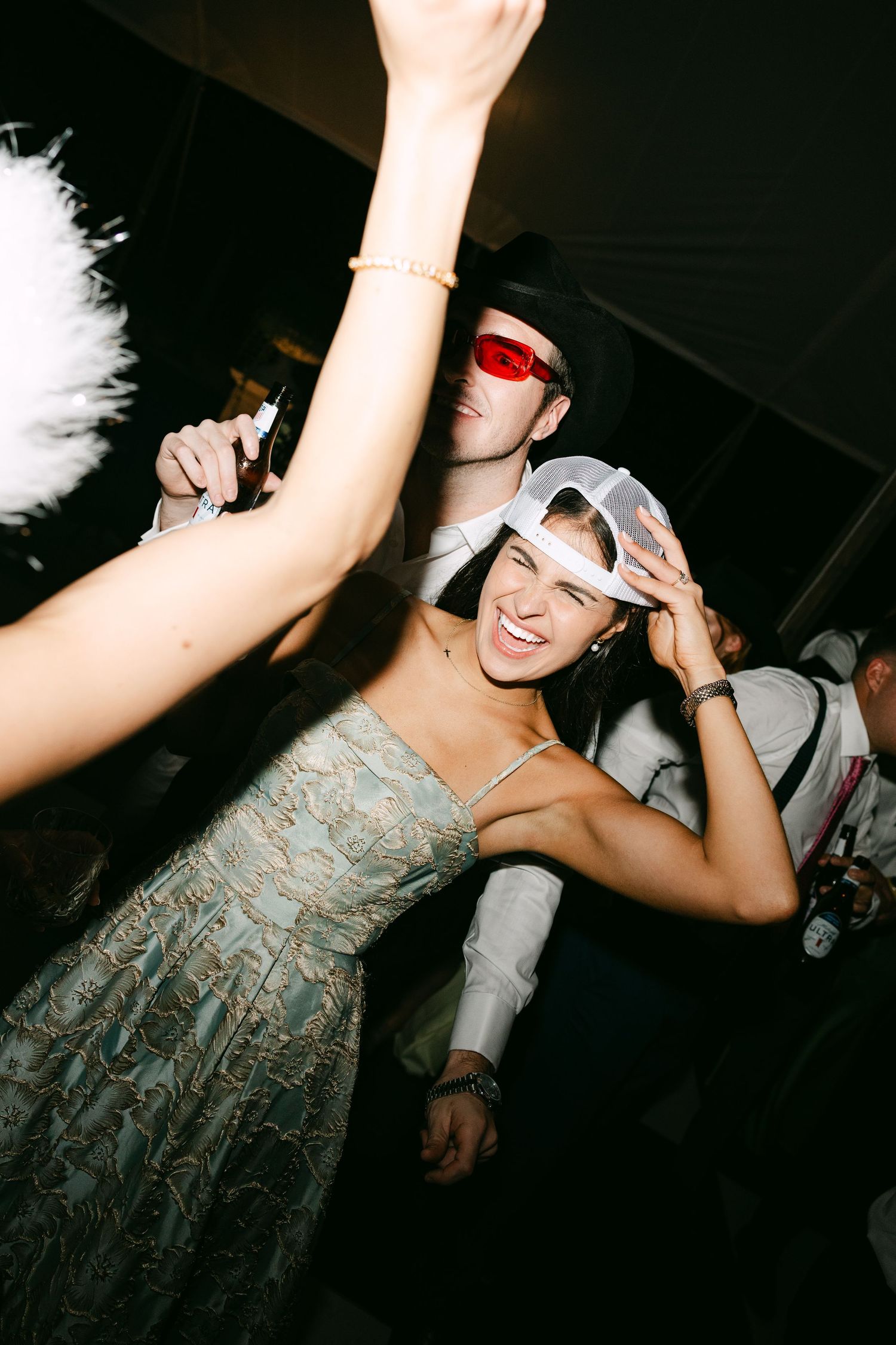 Guests dancing joyfully at a wedding reception, wearing fun accessories including colored glasses and a white cap.