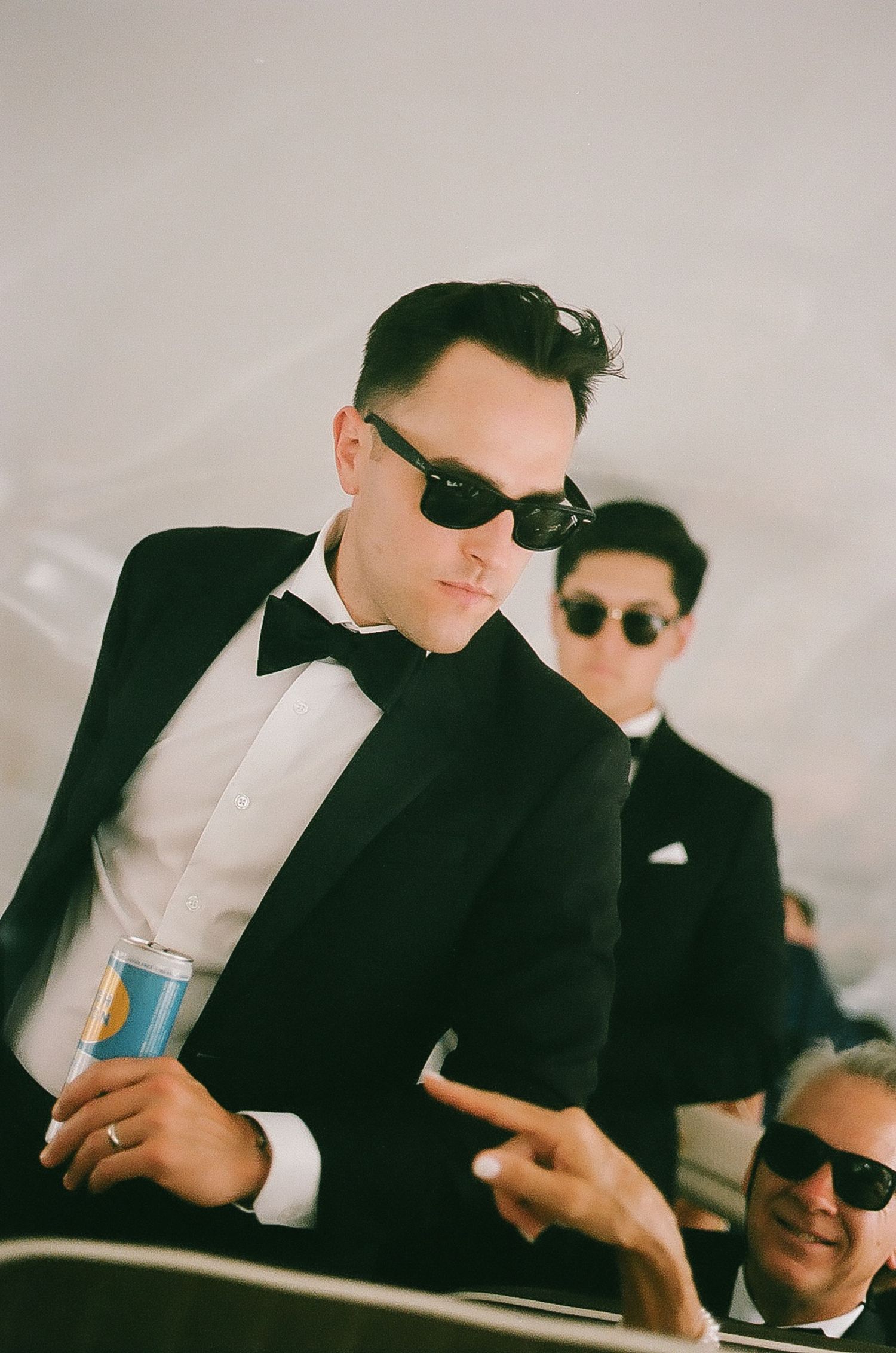 Wedding party members in black suits relax with drinks at reception.