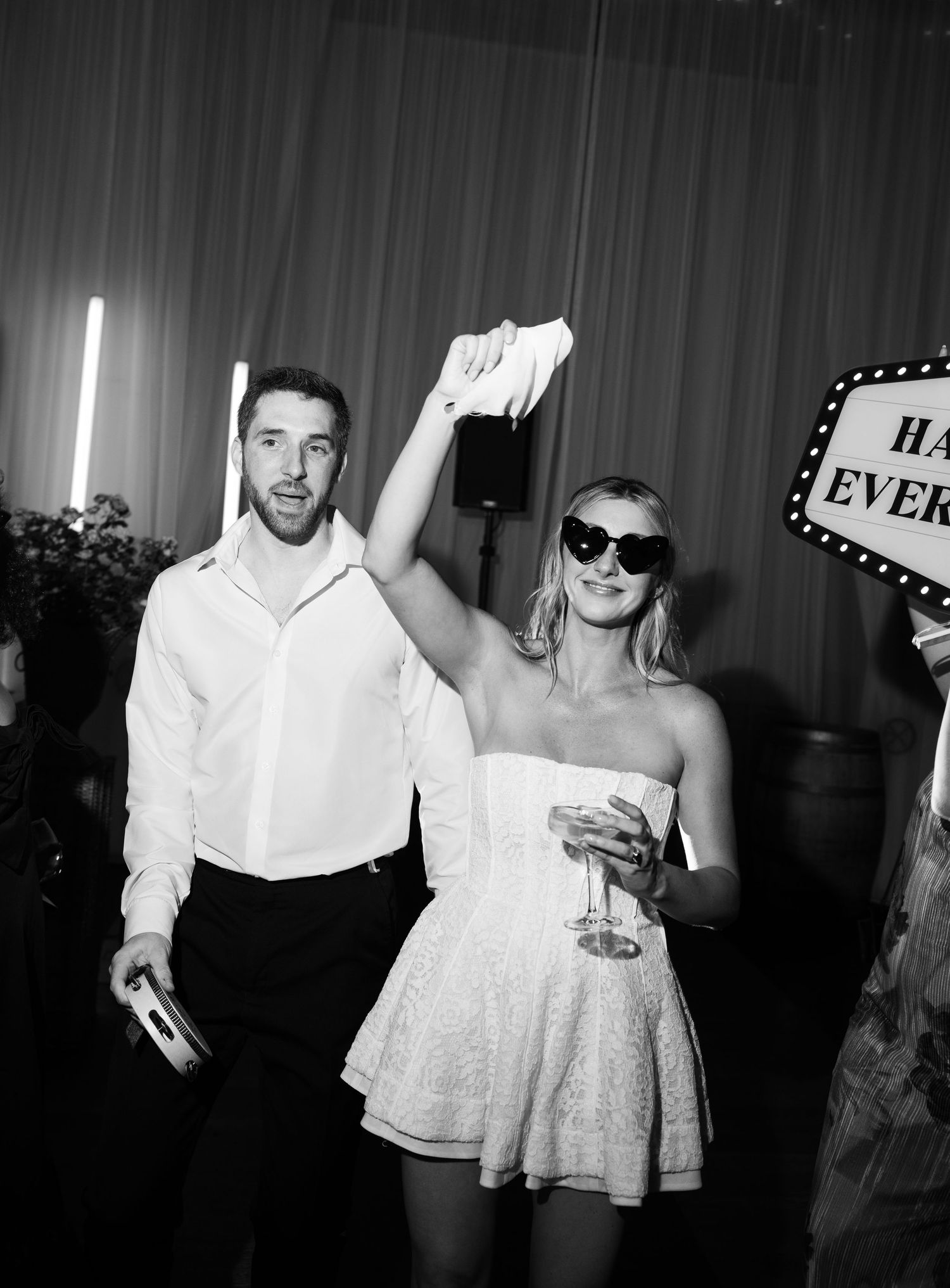 Black and white photo of bride in mini dress with sunglasses celebrating at wedding after party.