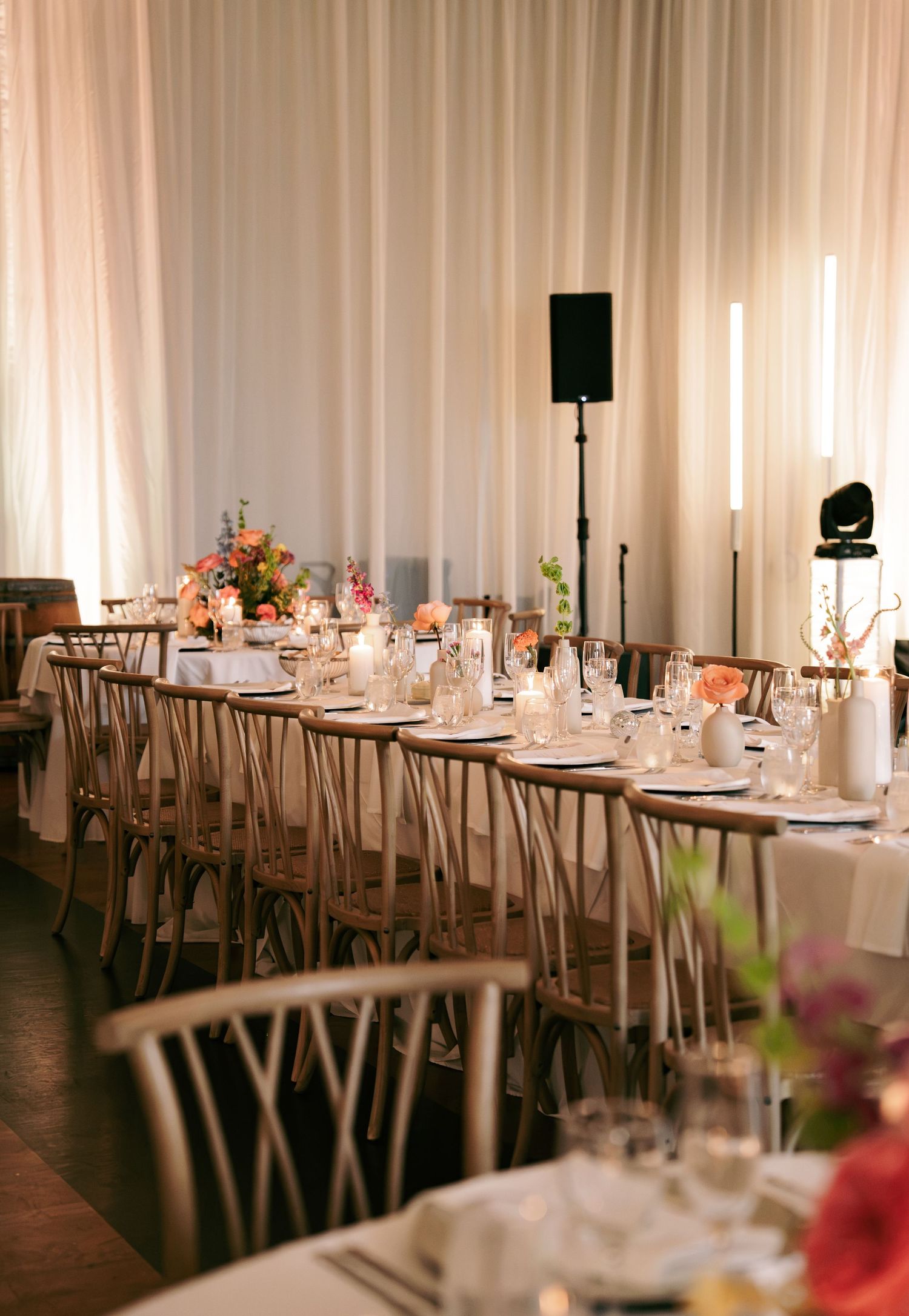 Romantic wedding reception with long tables, cross-back chairs, candles and colorful floral arrangements.