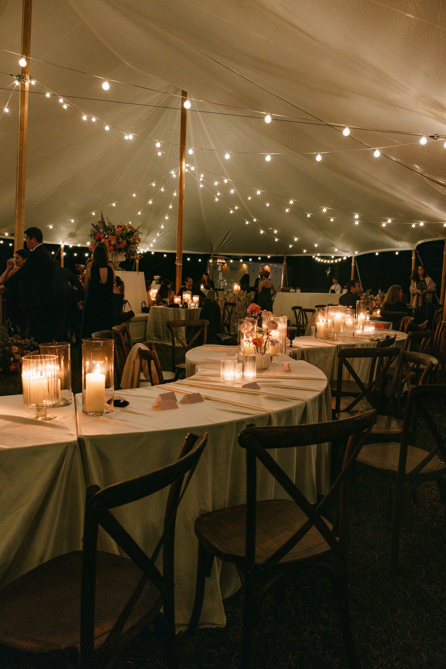 Elegant wedding reception inside a sperry tent with string lights, candles, and round tables at night.
