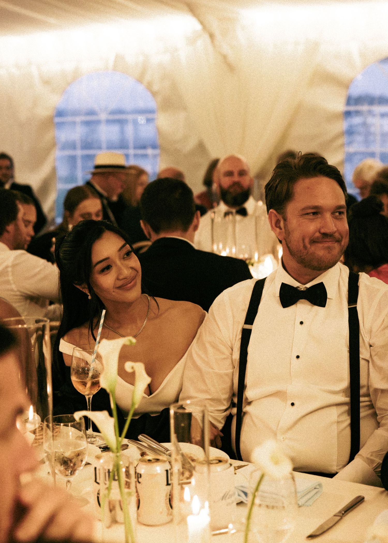 Bride and groom share a joyful moment at their candlelit wedding reception dinner under a white tent.