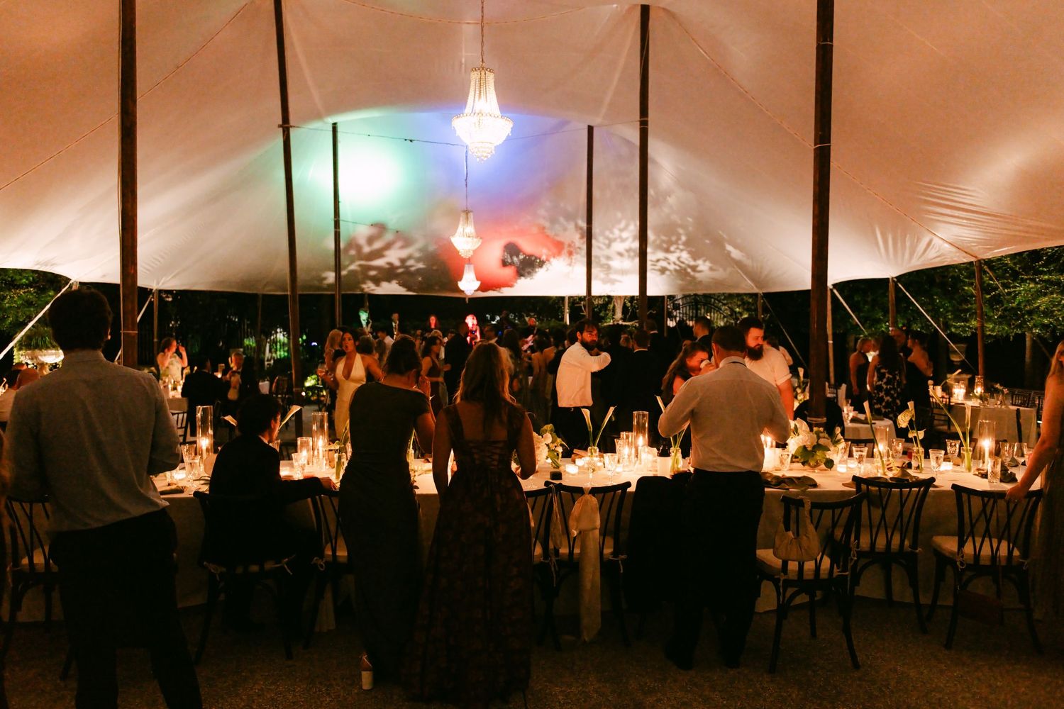 Guests dancing and celebrating under a white tent at an elegant evening wedding reception.