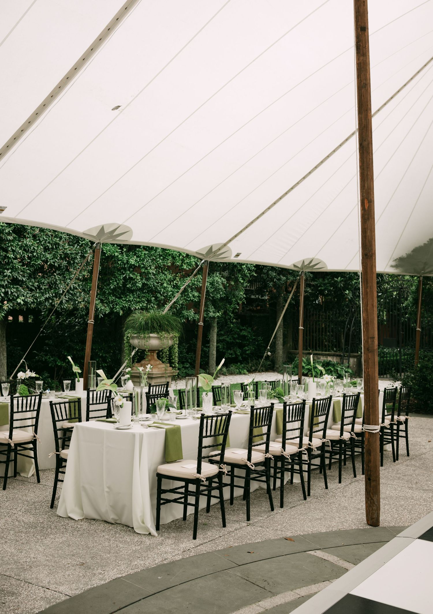 Elegant outdoor wedding reception under a white sailcloth tent with long tables, black chiavari chairs, and green floral centerpieces.