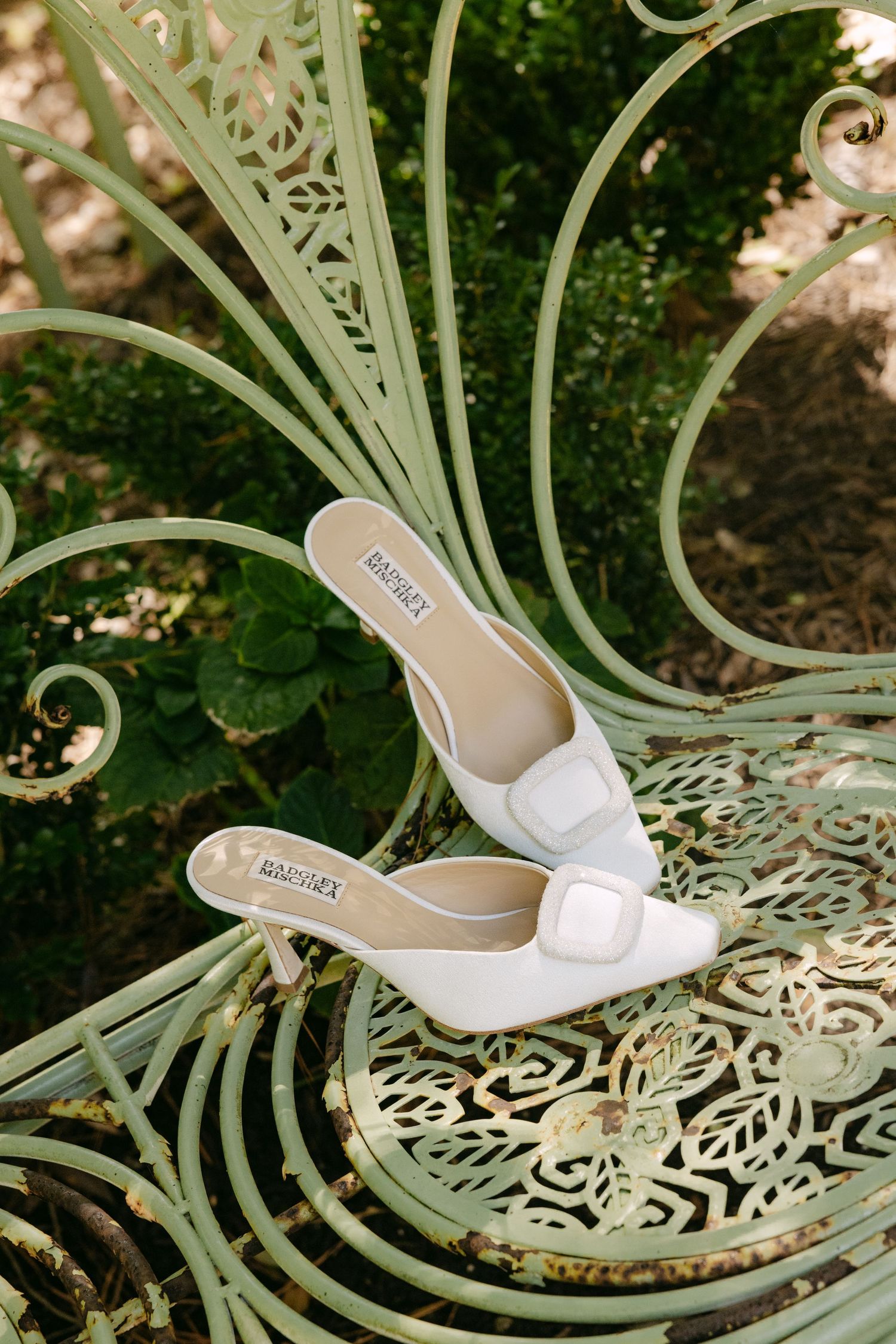 White bridal shoes displayed on an ornate mint green metal garden furniture with intricate scrollwork pattern.