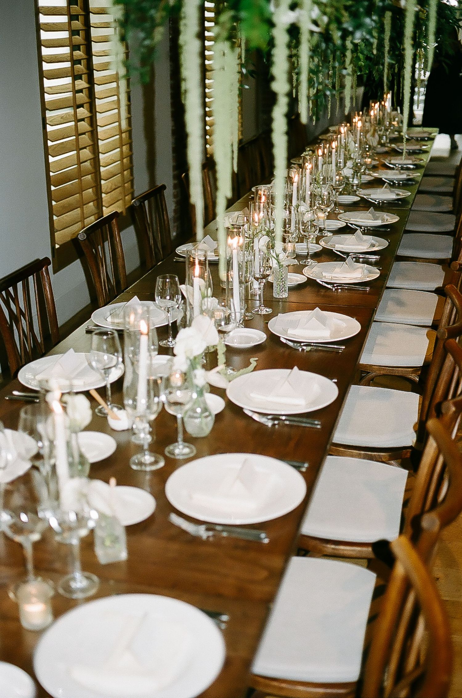 Long wooden dining table set with formal place settings and glassware.