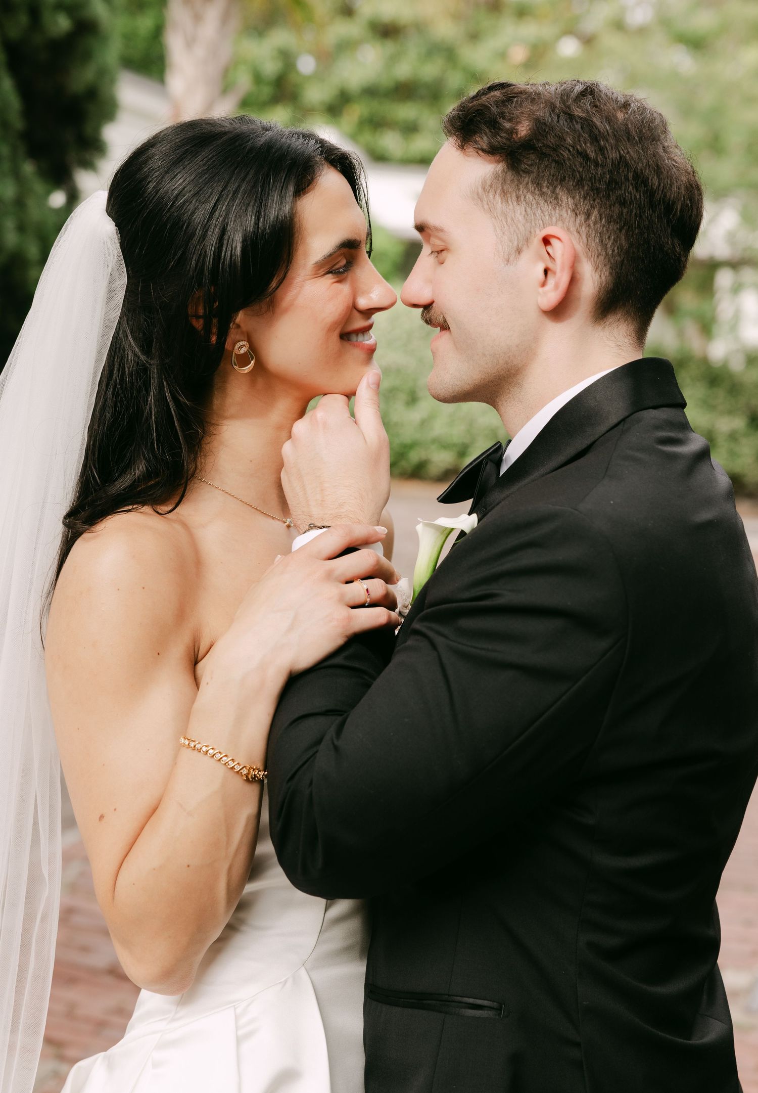 Bride and groom sharing romantic moment, nearly kissing outdoors on their wedding day.
